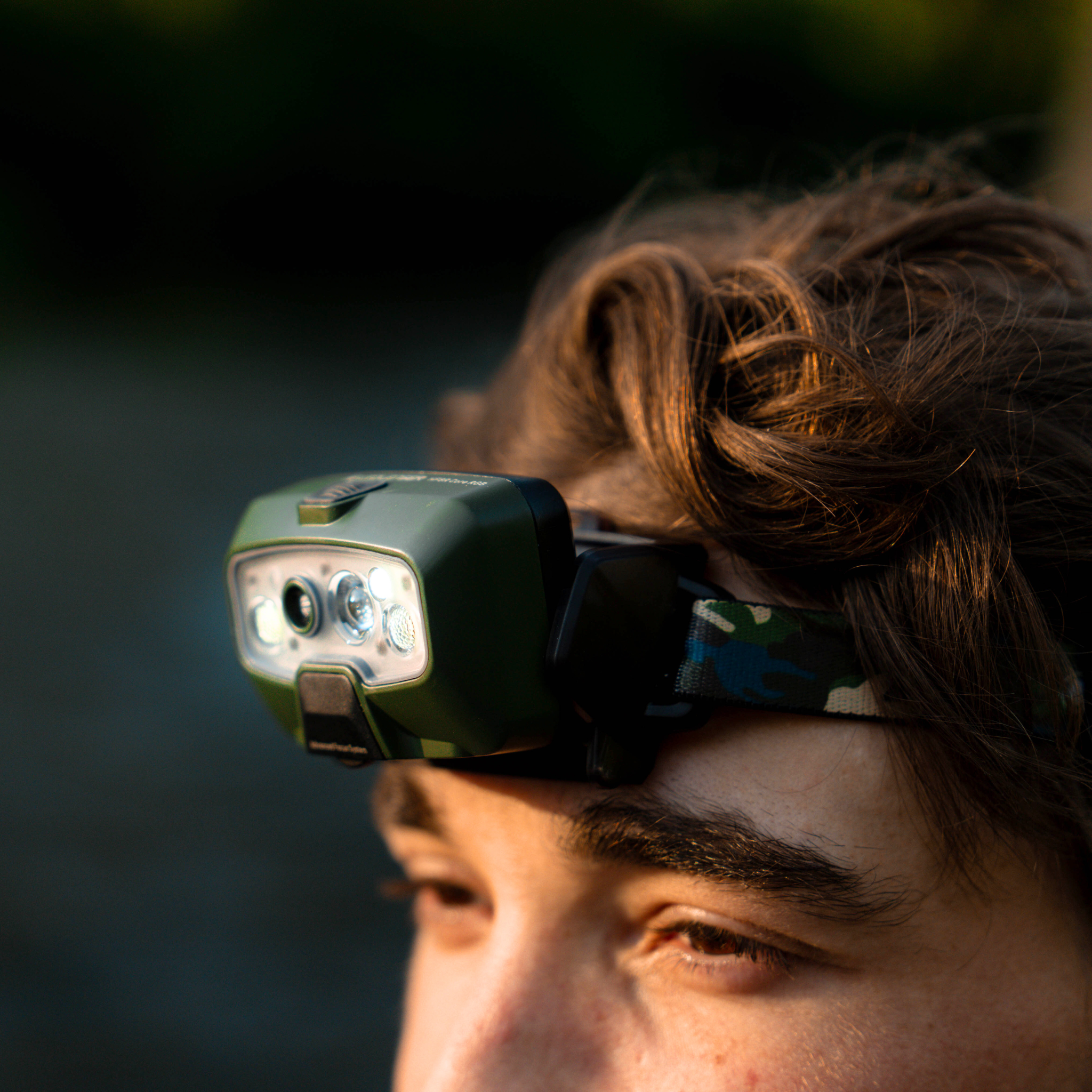 HF8R Core RGB Camo headlamp worn on a camo strap across the forehead angled side view showing green body and multiple LEDs