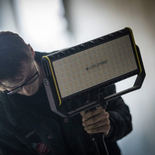 AF12R Work Floodlight held on a stand by a person showing a rectangular LED panel with yellow trim and Ledlenser branding
