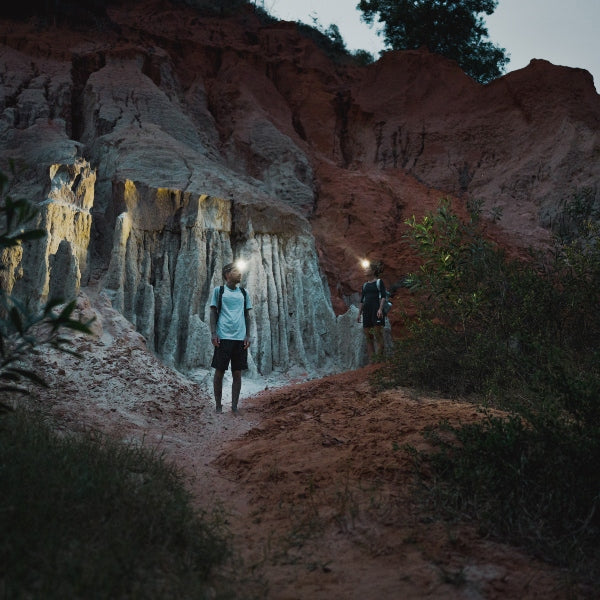 HF6R Signature Headlamp worn by a hiker in a rocky canyon at dusk; two walkers with headlamps illuminating the trail