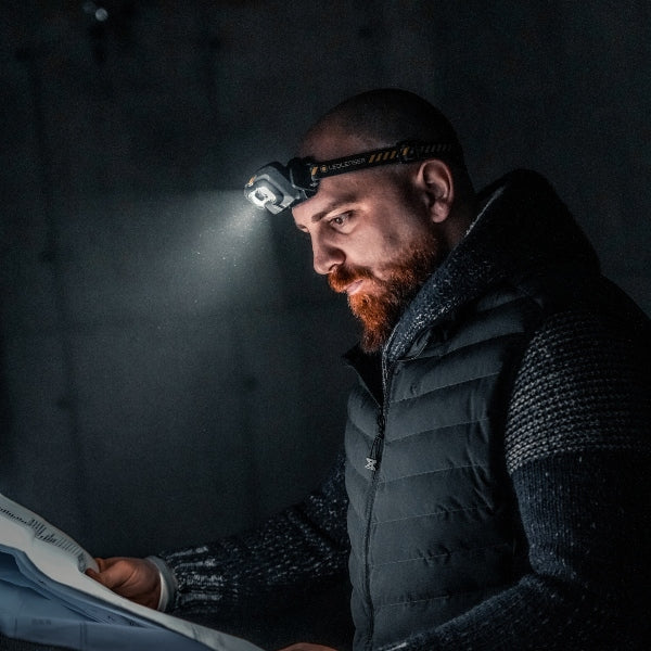 HF8R Work Headlamp worn by a bearded man in a dark jacket reading a document with the headlamp beam illuminating the page