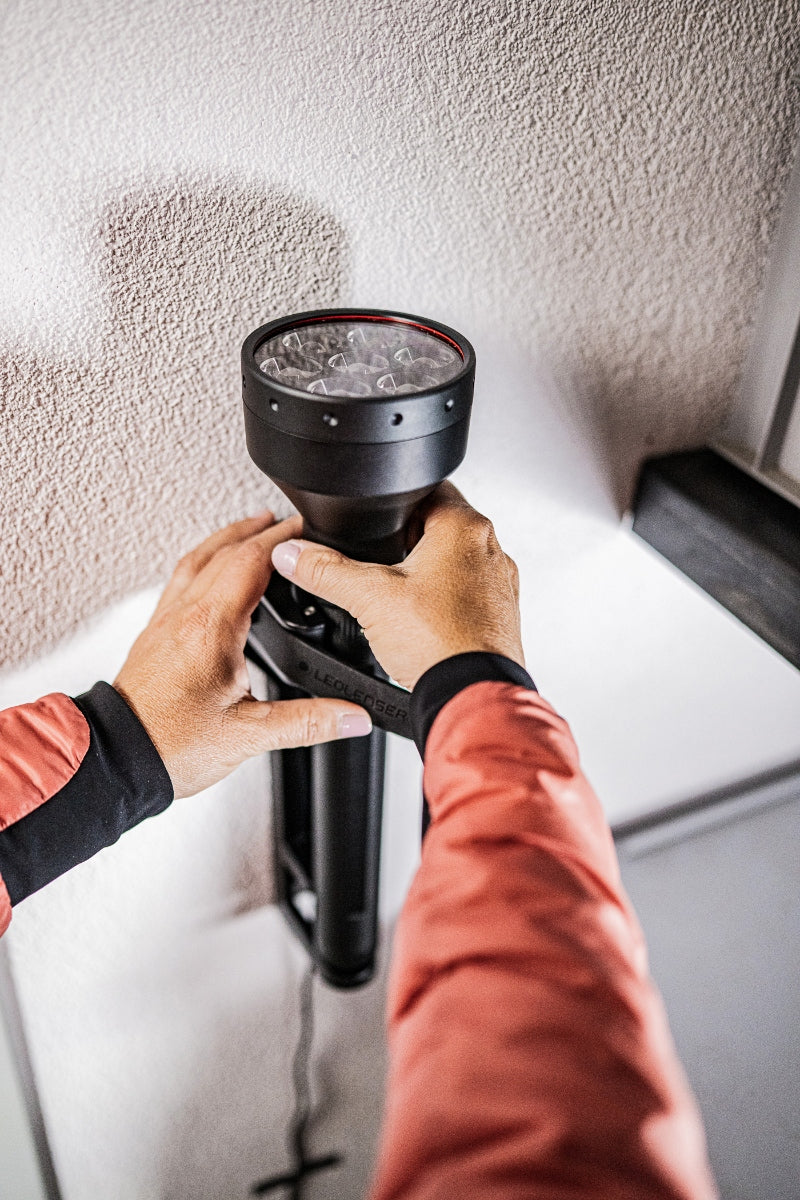 P21R Torch held by hands a black rechargeable flashlight with a large head against a textured wall