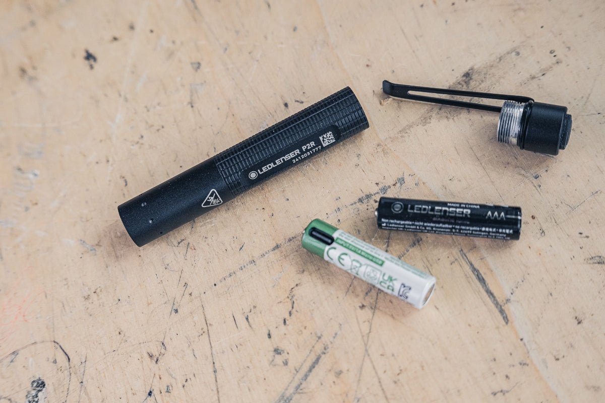 P2R Torch by Ledlenser disassembled with replaceable battery and end cap on a wooden work surface