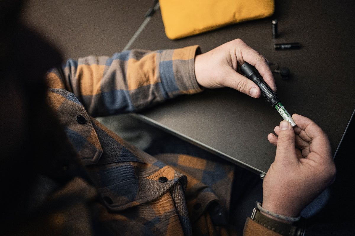 Ledlenser P3R Torch being assembled by a person in a plaid shirt inserting a battery into the rechargeable flashlight