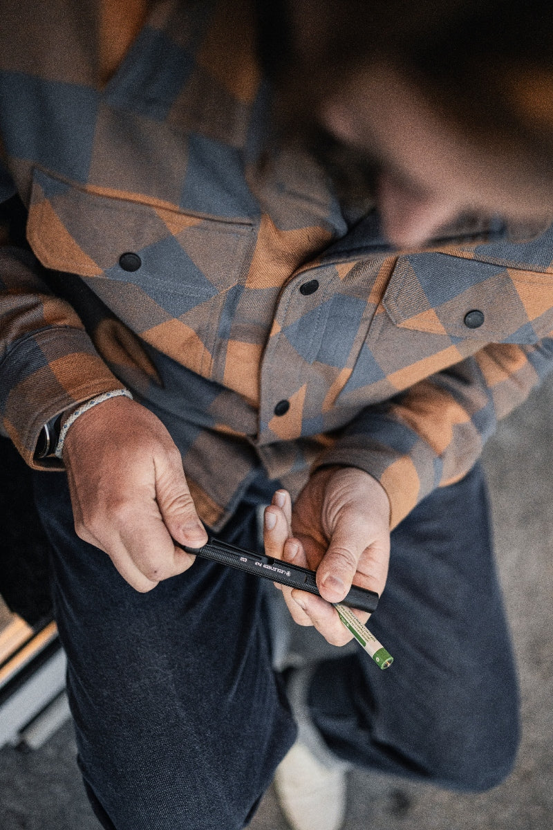 P4R Torch held in hands black pen style flashlight with green tip worn with a blue orange plaid shirt