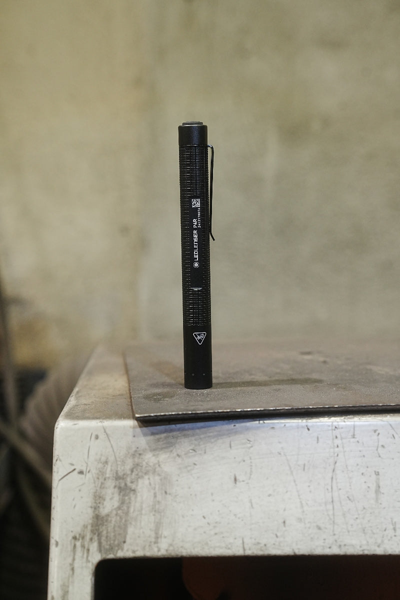 P4R Torch by Ledlenser black cylindrical pocket flashlight with clip standing upright on a metal workbench