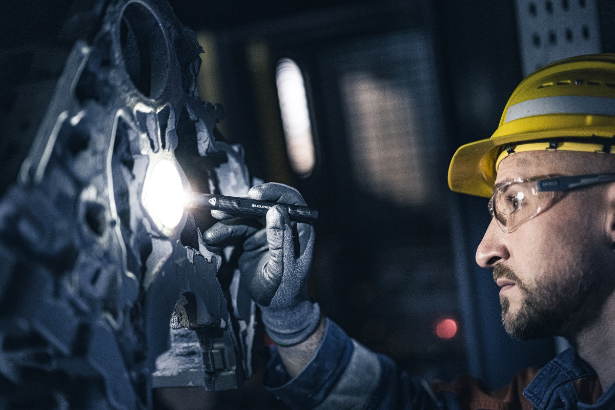 P4R Torch held by a safety worker in a yellow hard hat and goggles illuminating a large industrial machine from the side