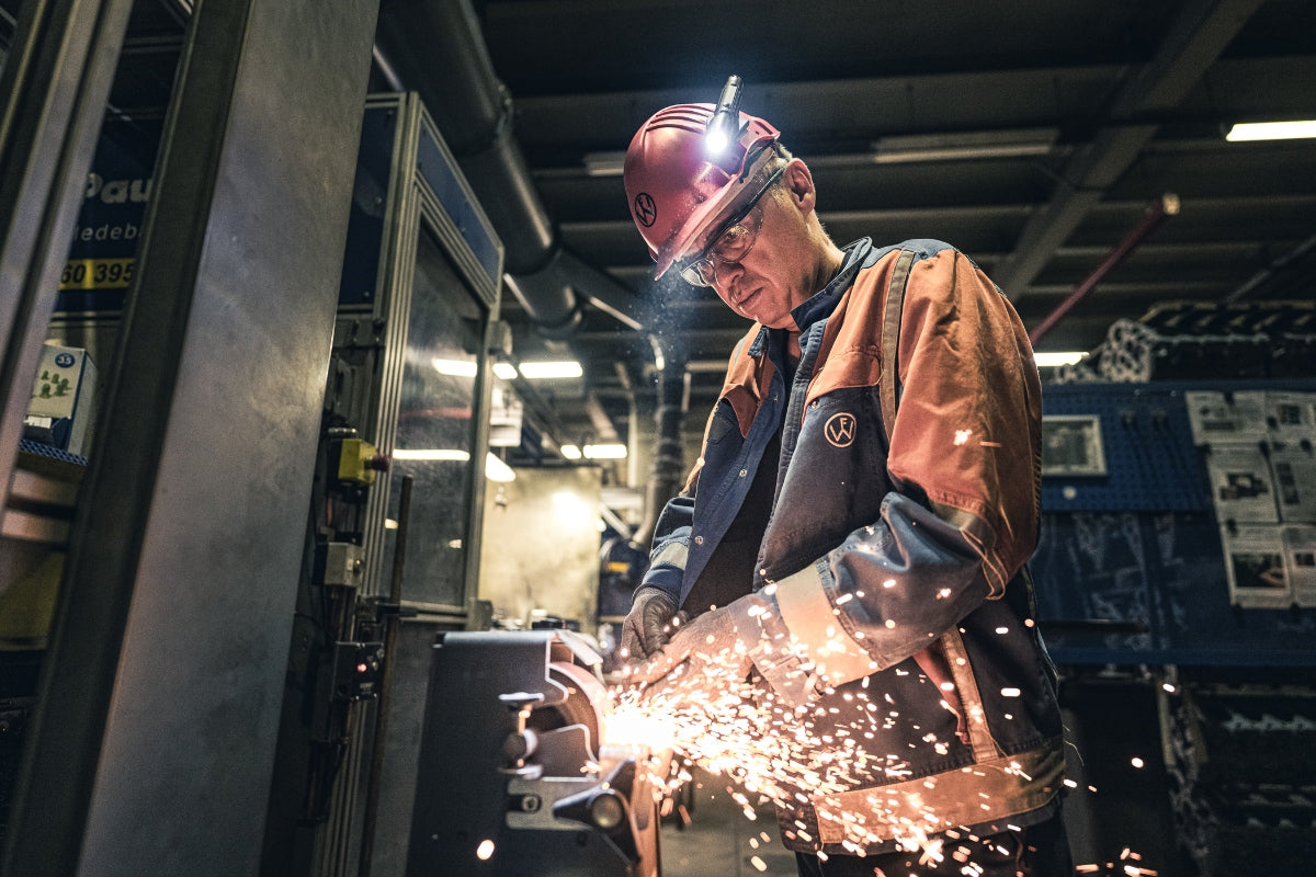 Ledlenser P5R Torch worn by a worker with a headlamp on a helmet in an industrial workshop with welding sparks