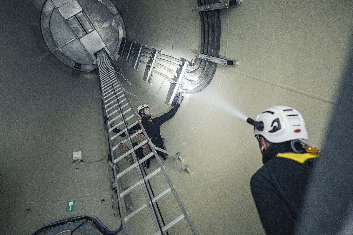 P5R Torch being used inside an industrial shaft with a worker on a ladder wearing a helmet and headlamp projecting light toward the wall