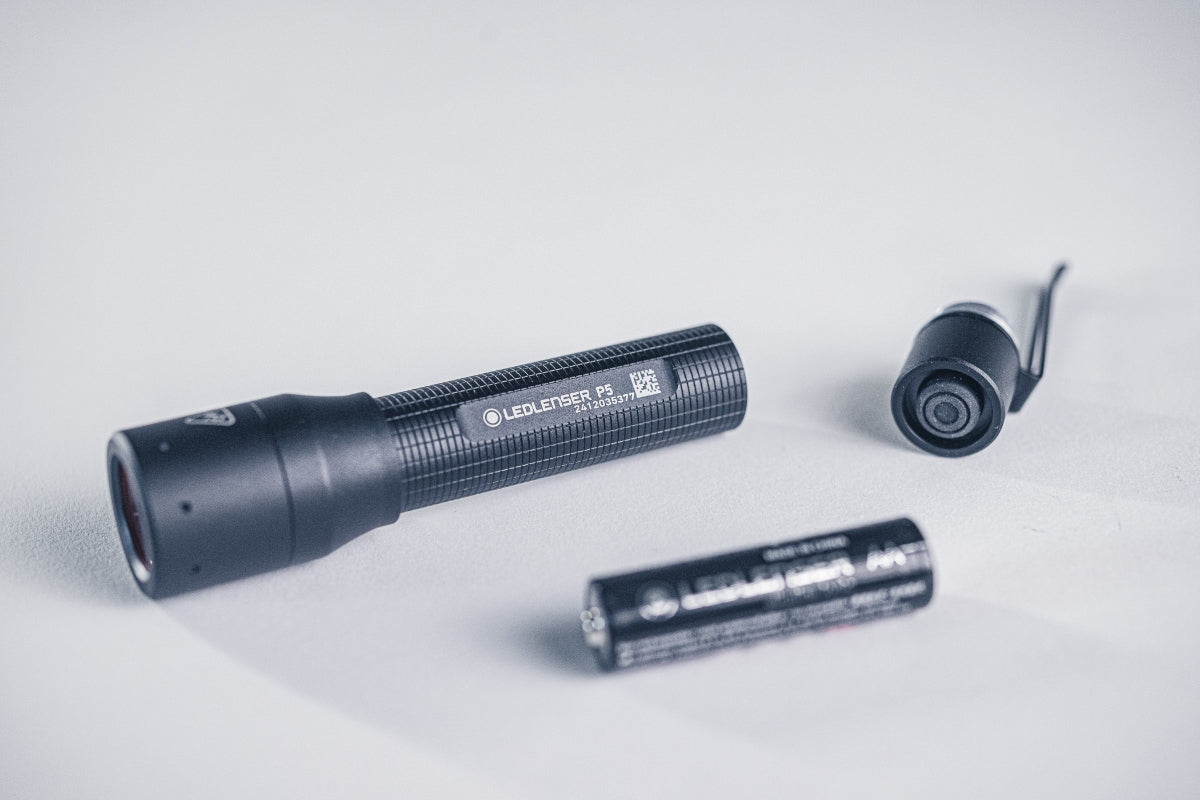 Ledlenser P5 Torch disassembled showing body tube AA battery and end cap with clip on a light surface