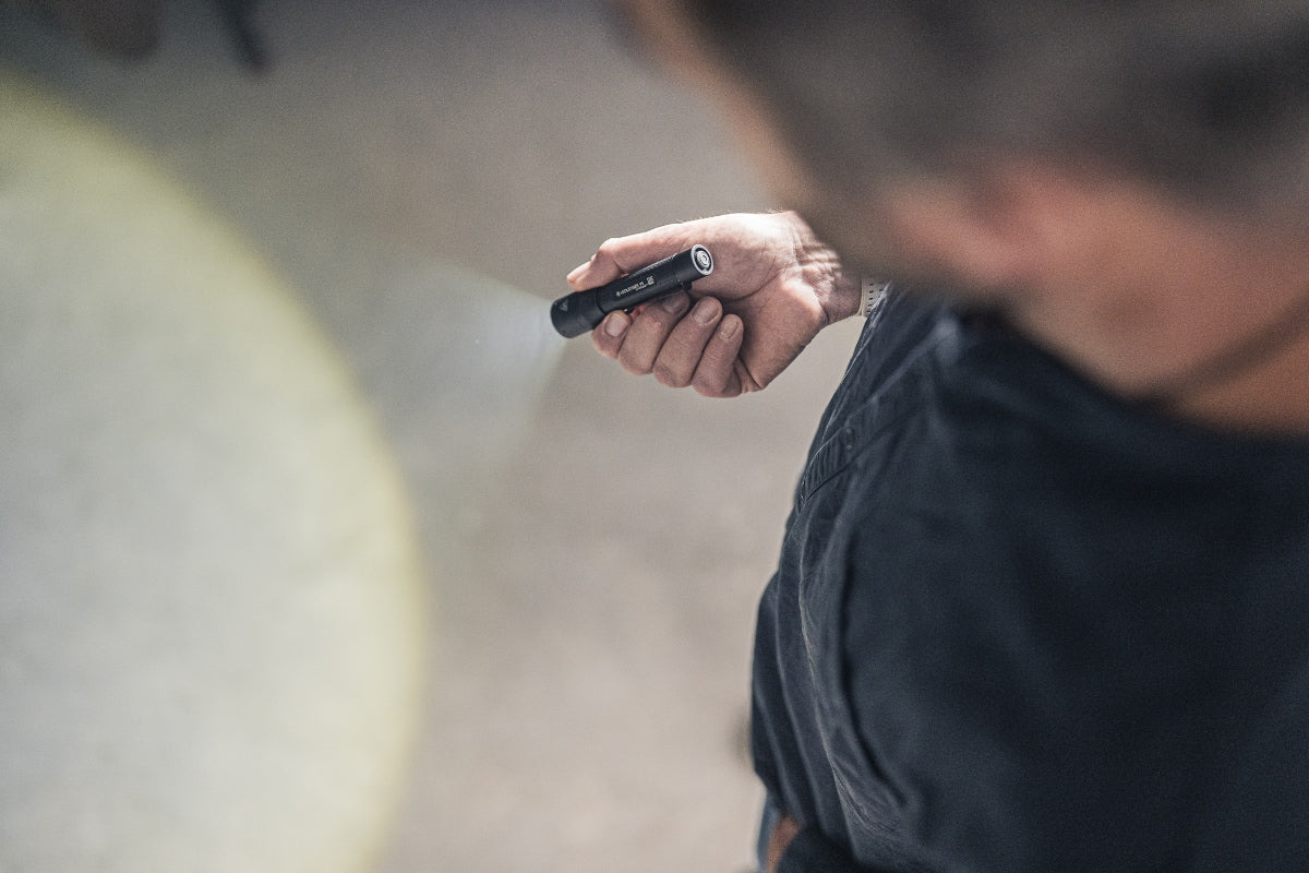 Ledlenser P5 Torch held in a right hand compact flashlight with beam projecting forward in an outdoor setting