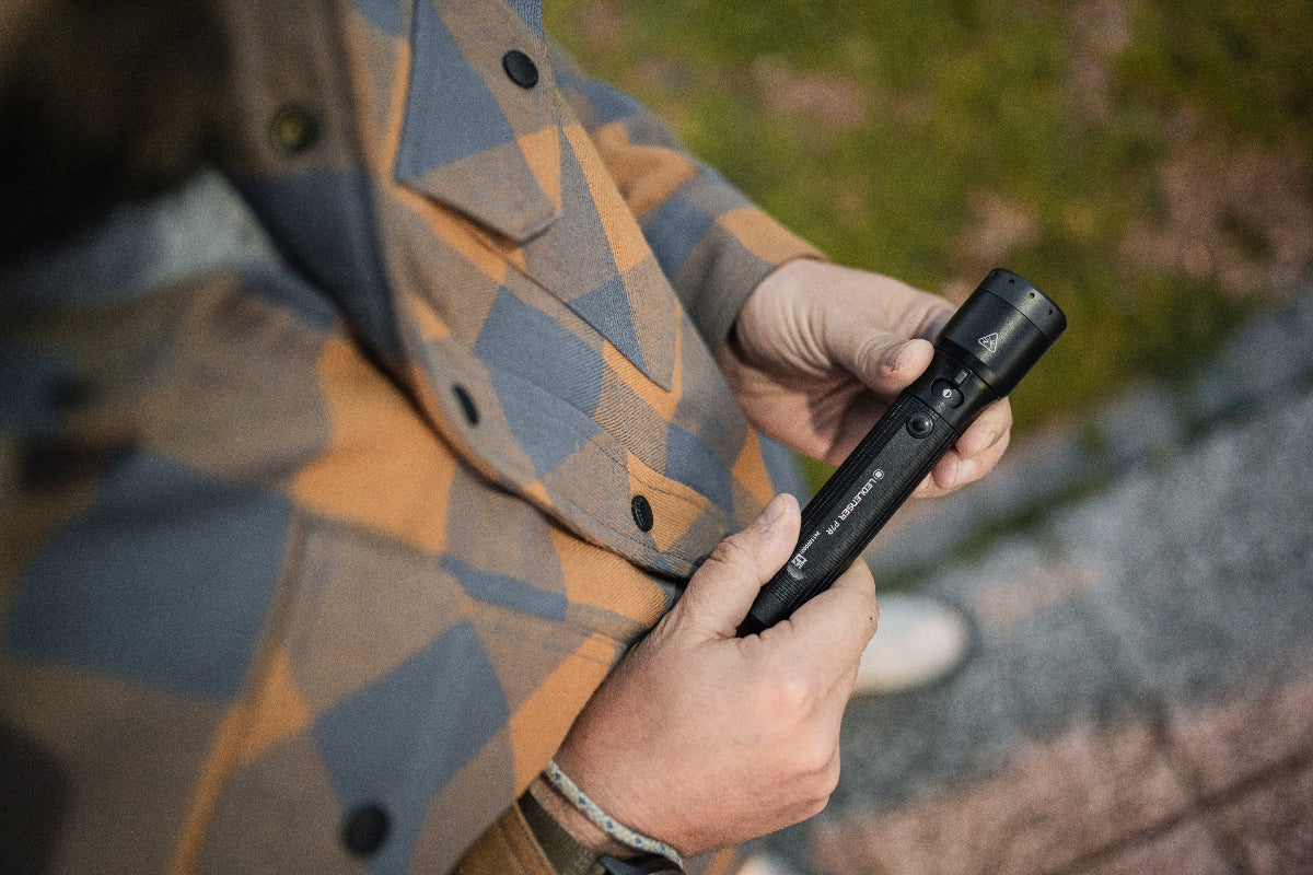 Ledlenser P7R Torch held in hands outdoors black compact rechargeable flashlight with textured grip plaid jacket in background