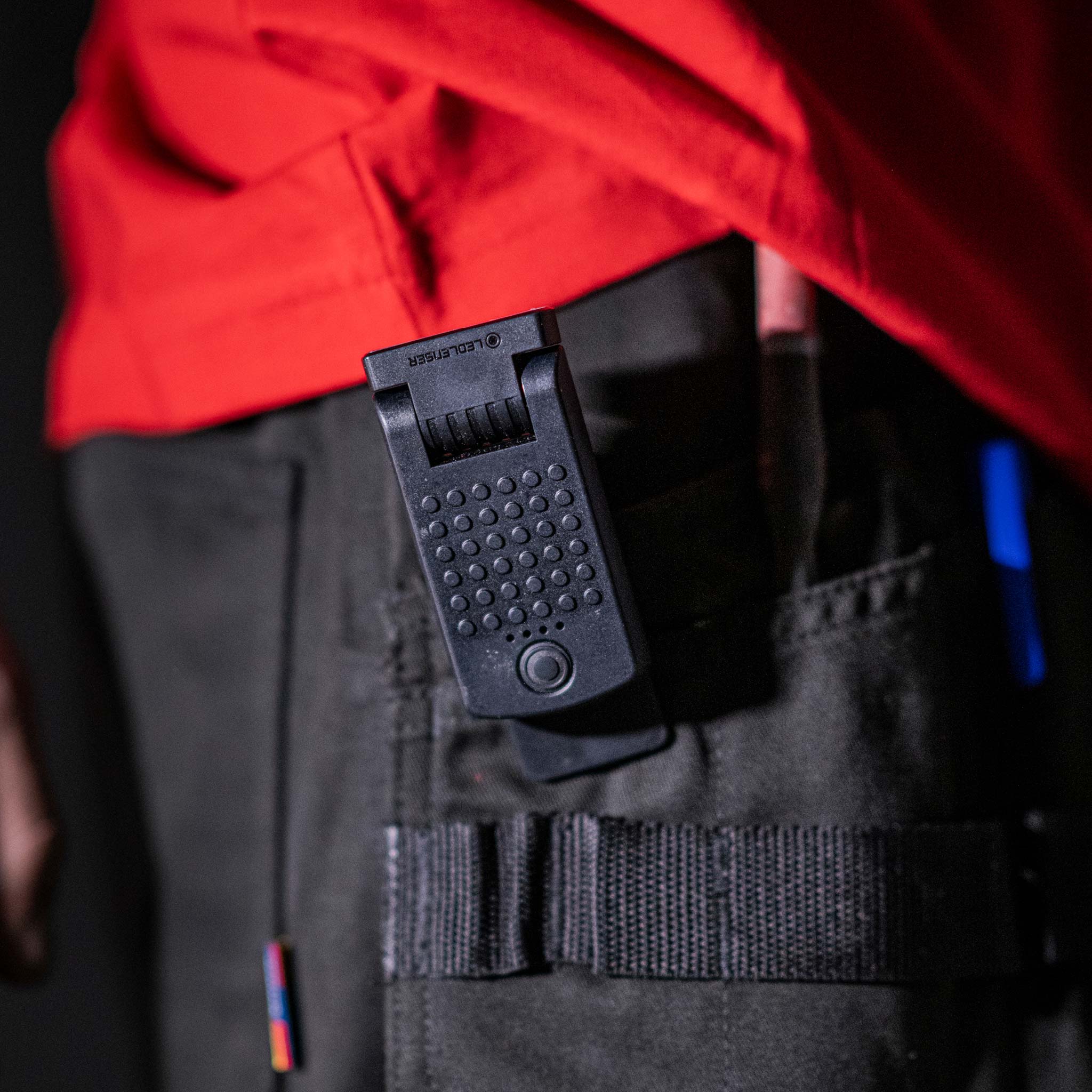 Ledlenser W1R Work Clip Light clipped to a work belt with textured black housing and control button red jacket in background