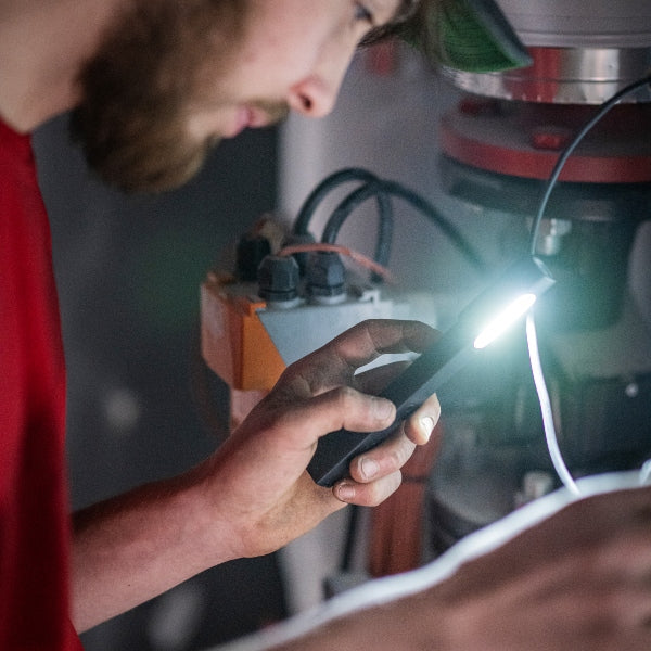 Ledlenser W2 Work Pen and Test Light being held in a hand with the light on in a workshop setting