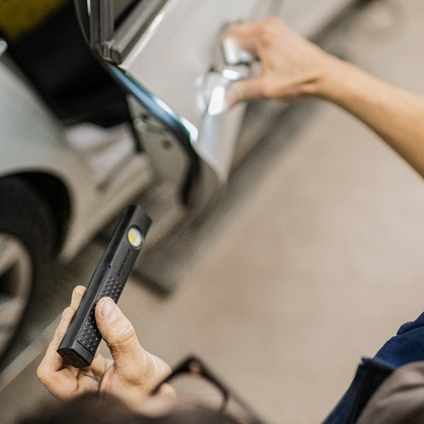 Ledlenser W4R Work Worklight held in hand illuminating a car door area during maintenance; compact black rectangular torch