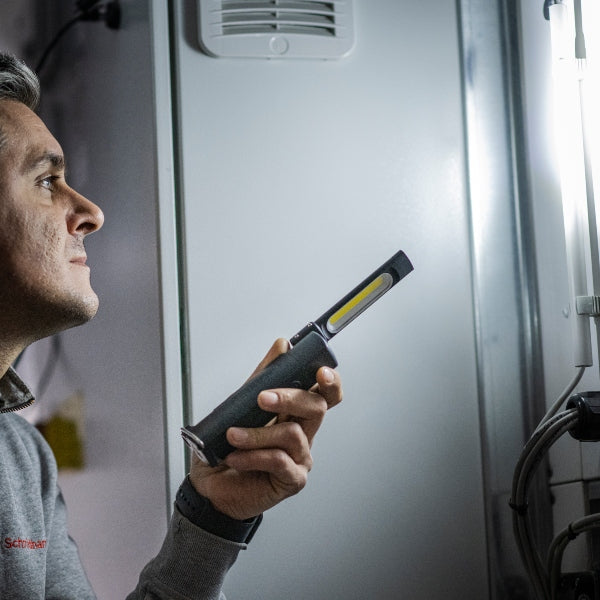 Ledlenser W6R Work Light held by a person in a workshop showing a compact black body with a fold out head and yellow LED strip