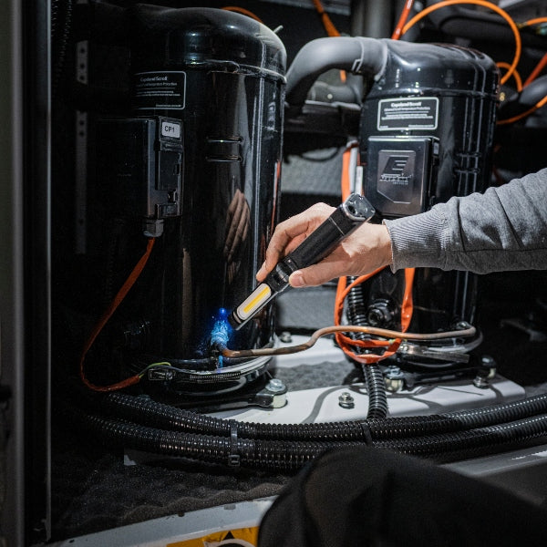 Ledlenser W7R Work Light being used handheld near industrial battery pods with orange cables; user in a gray sleeve operating the light