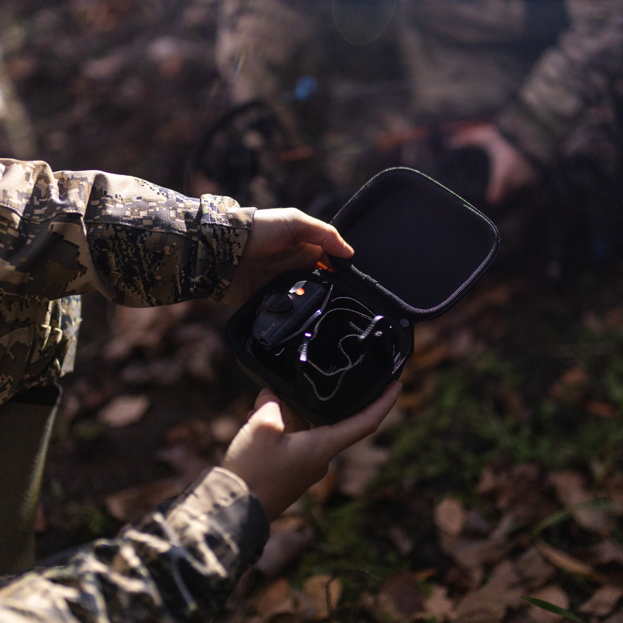 Ledlenser MH8 Powercase Combo headlamp and charging case being opened by hands in camouflage jacket outdoor forest setting