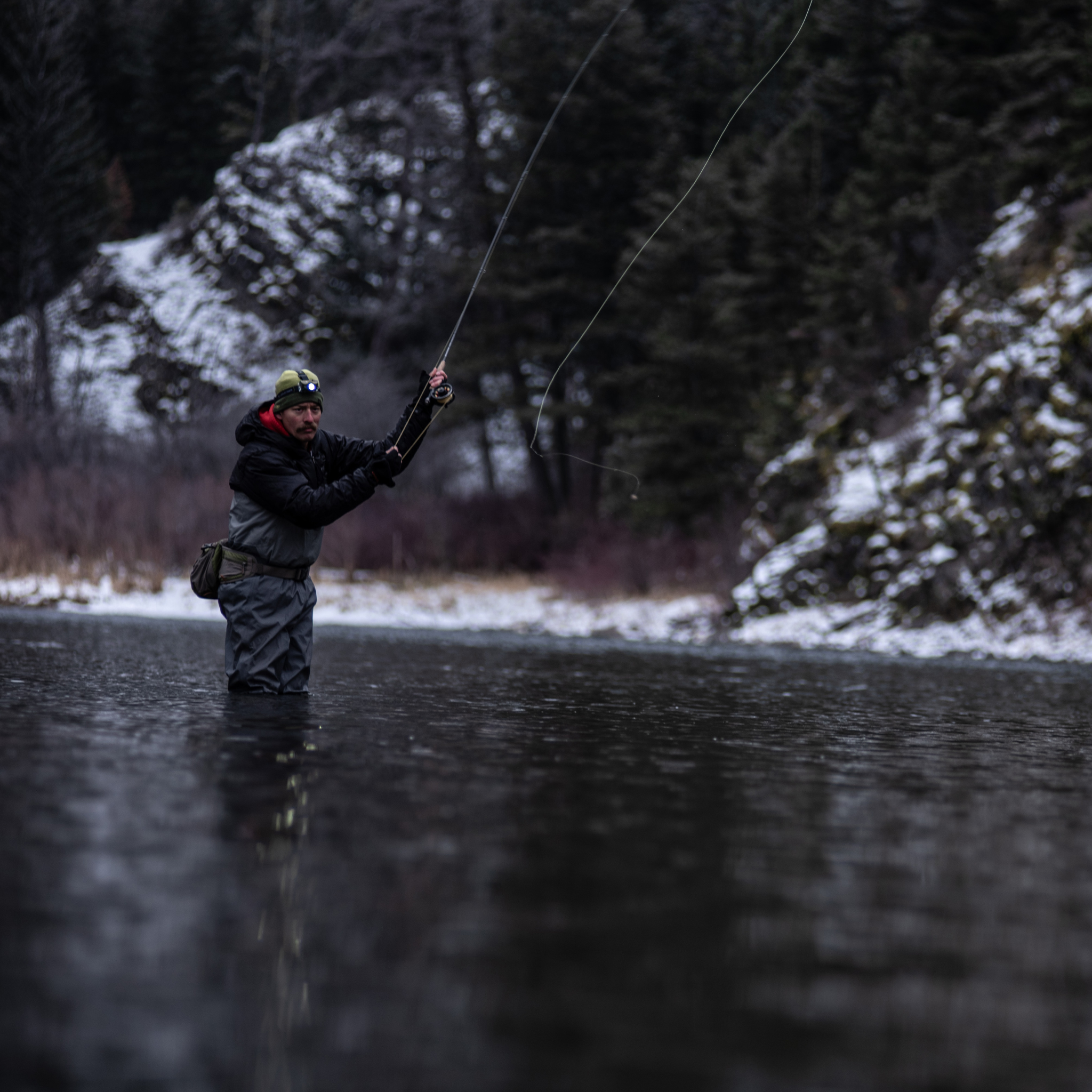 MH8 Outdoor Headlamp worn on the head by a man fishing in a river with snowy banks