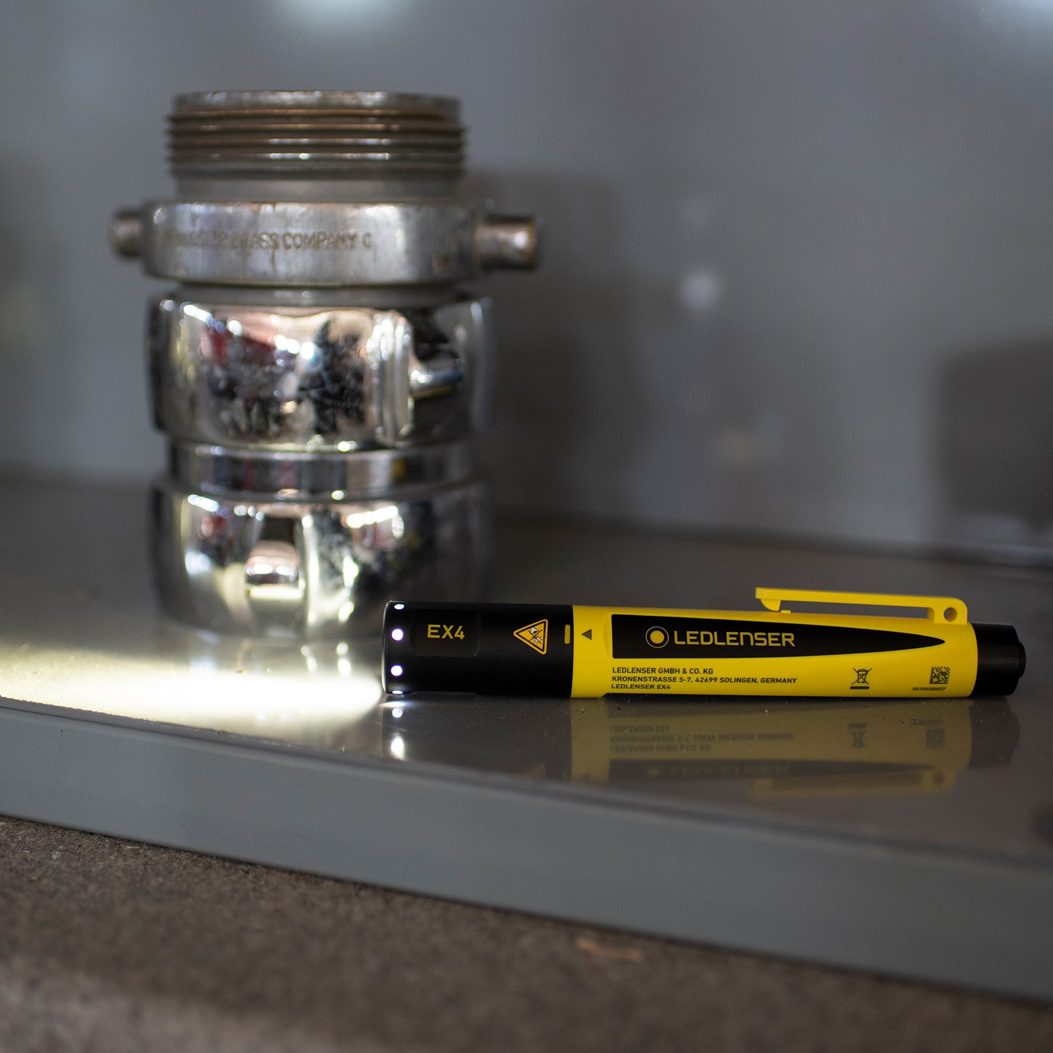 EX4 Torch by Ledlenser yellow and black handheld flashlight lying on a reflective surface with a metallic valve fitting in the background