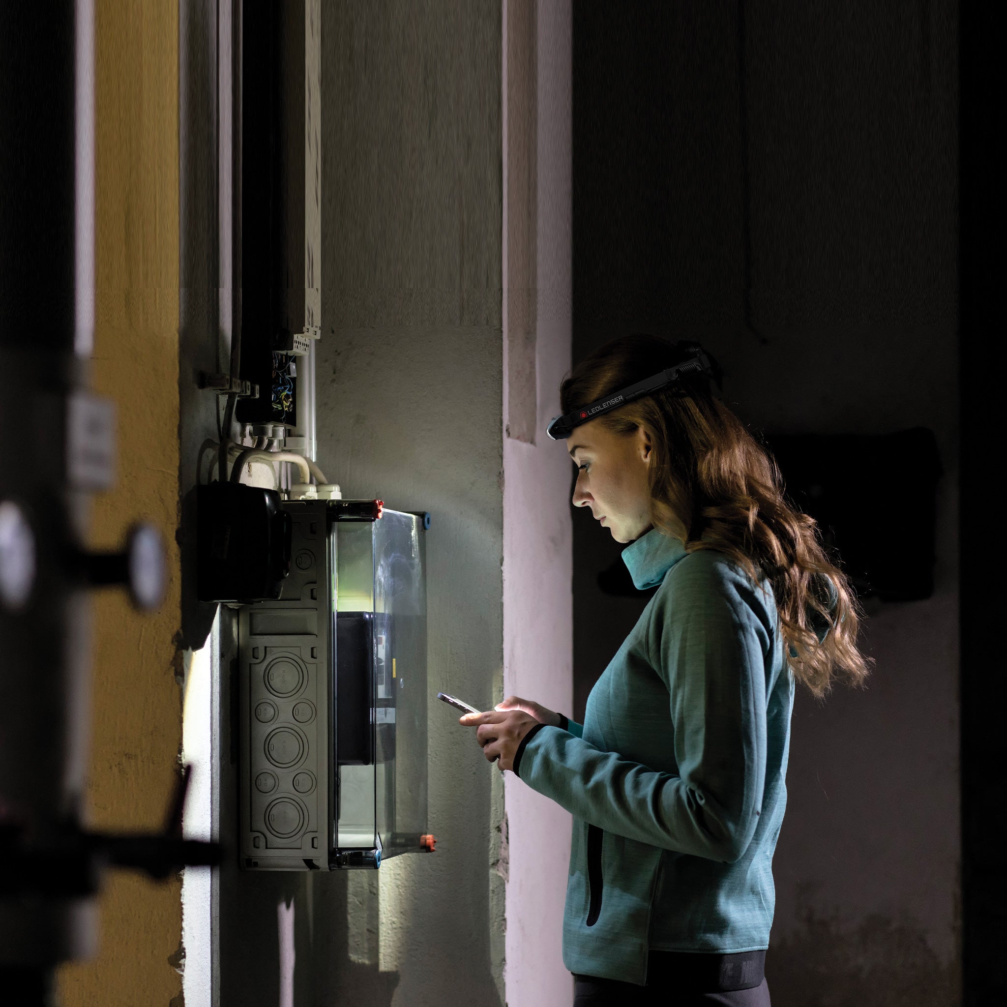 Ledlenser H4 Headlamp worn by a woman in a dim utility room inspecting an electrical panel with a focused beam