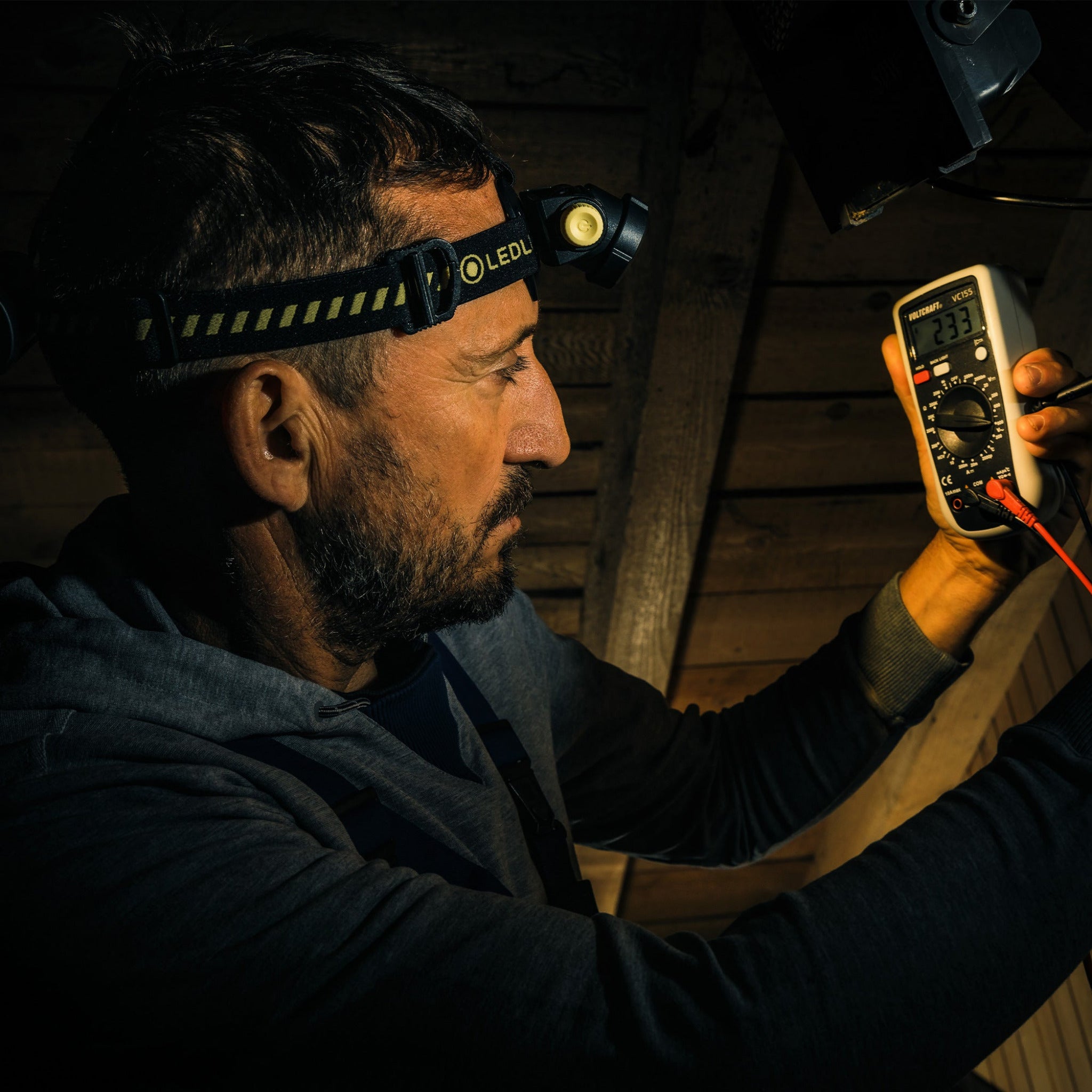 H5R Work Headlamp worn on a man’s head with a black Ledlenser headband in a dim wooden workshop