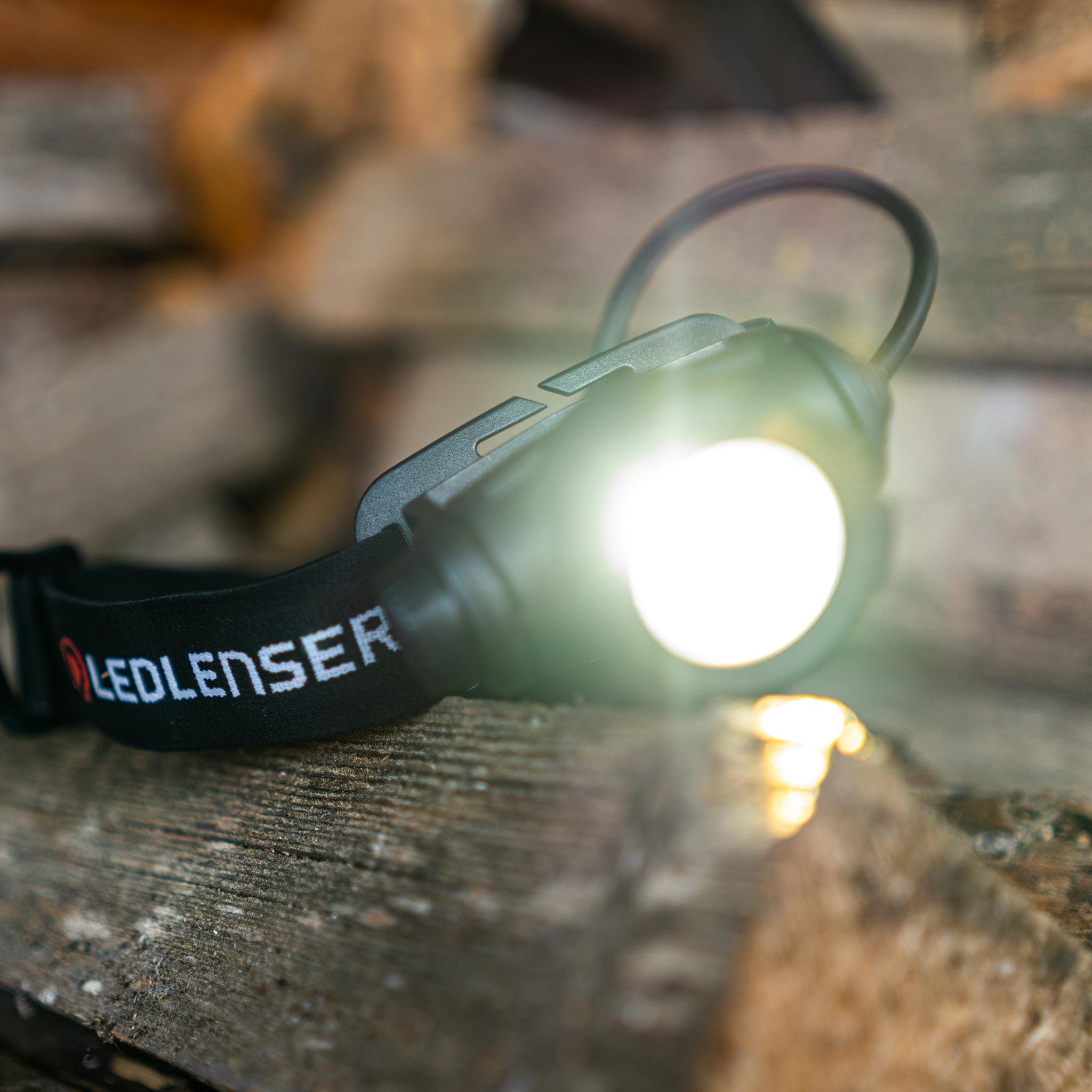 Ledlenser H7R Core headlamp with black adjustable strap showing the illuminated front light on a wooden surface