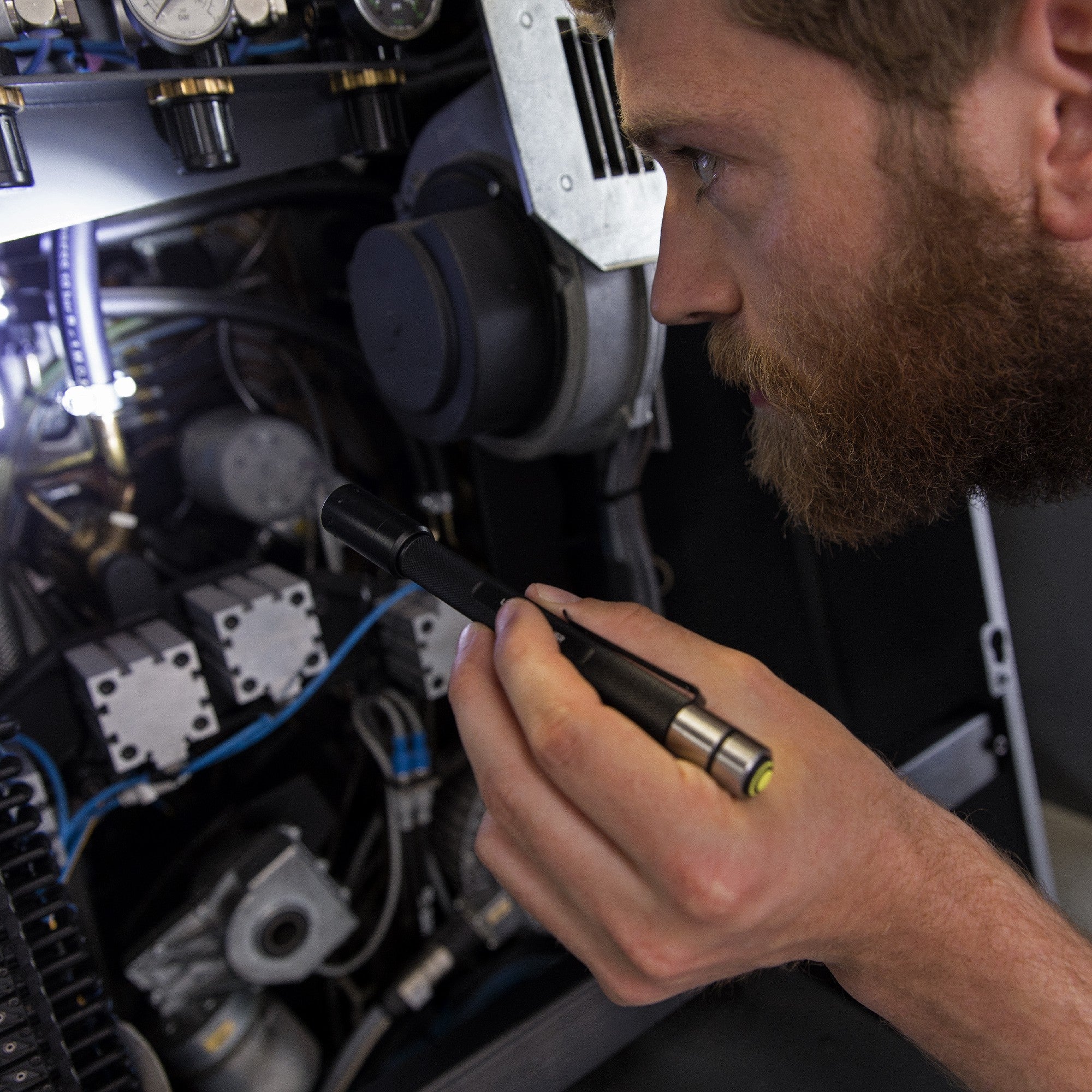 Technician holding a Ledlenser i6R Rechargeable Pen Light beside industrial machinery with gauges and wiring