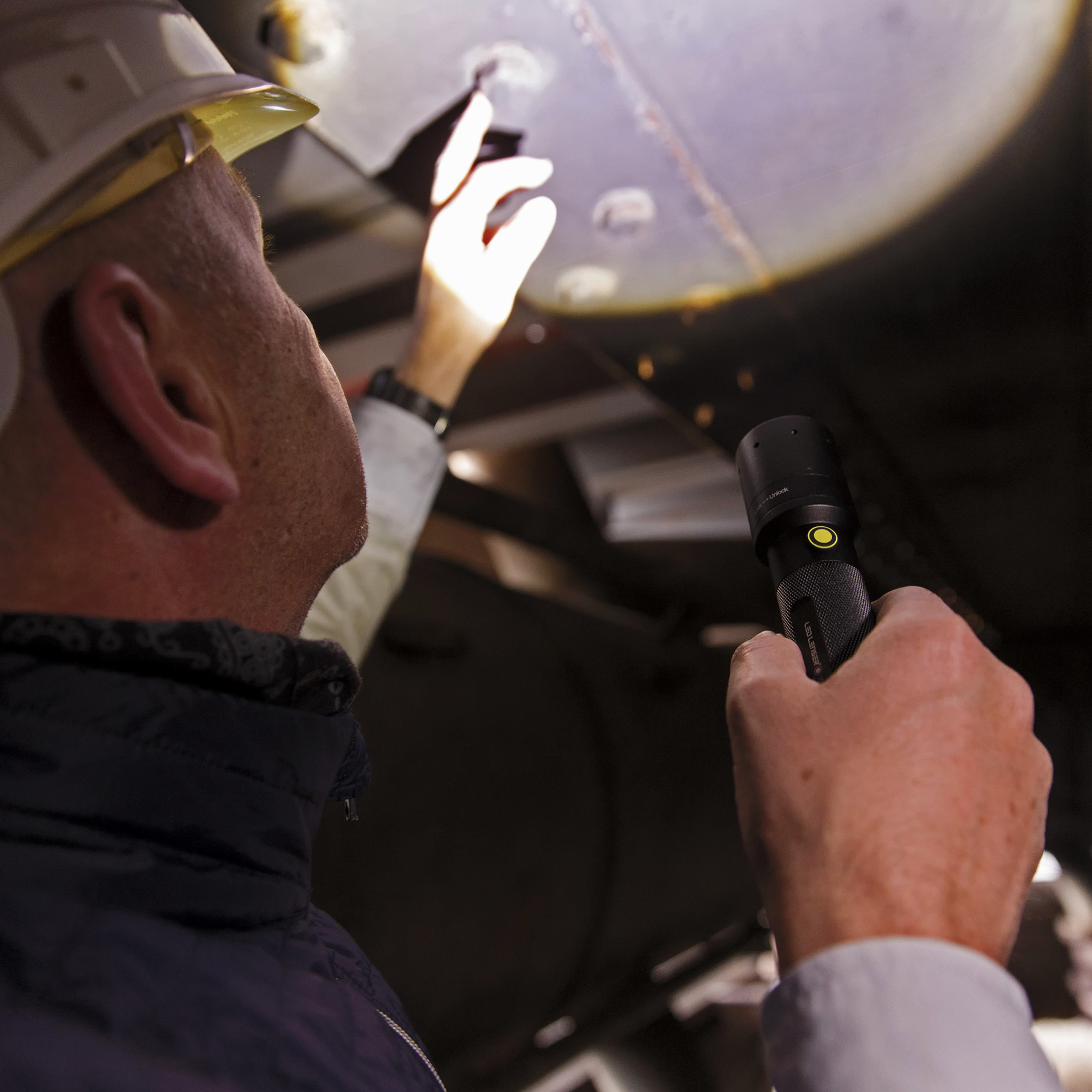 i9 CRI Torch held by a worker in a helmet close up of the tool aimed at an industrial ceiling panel during inspection