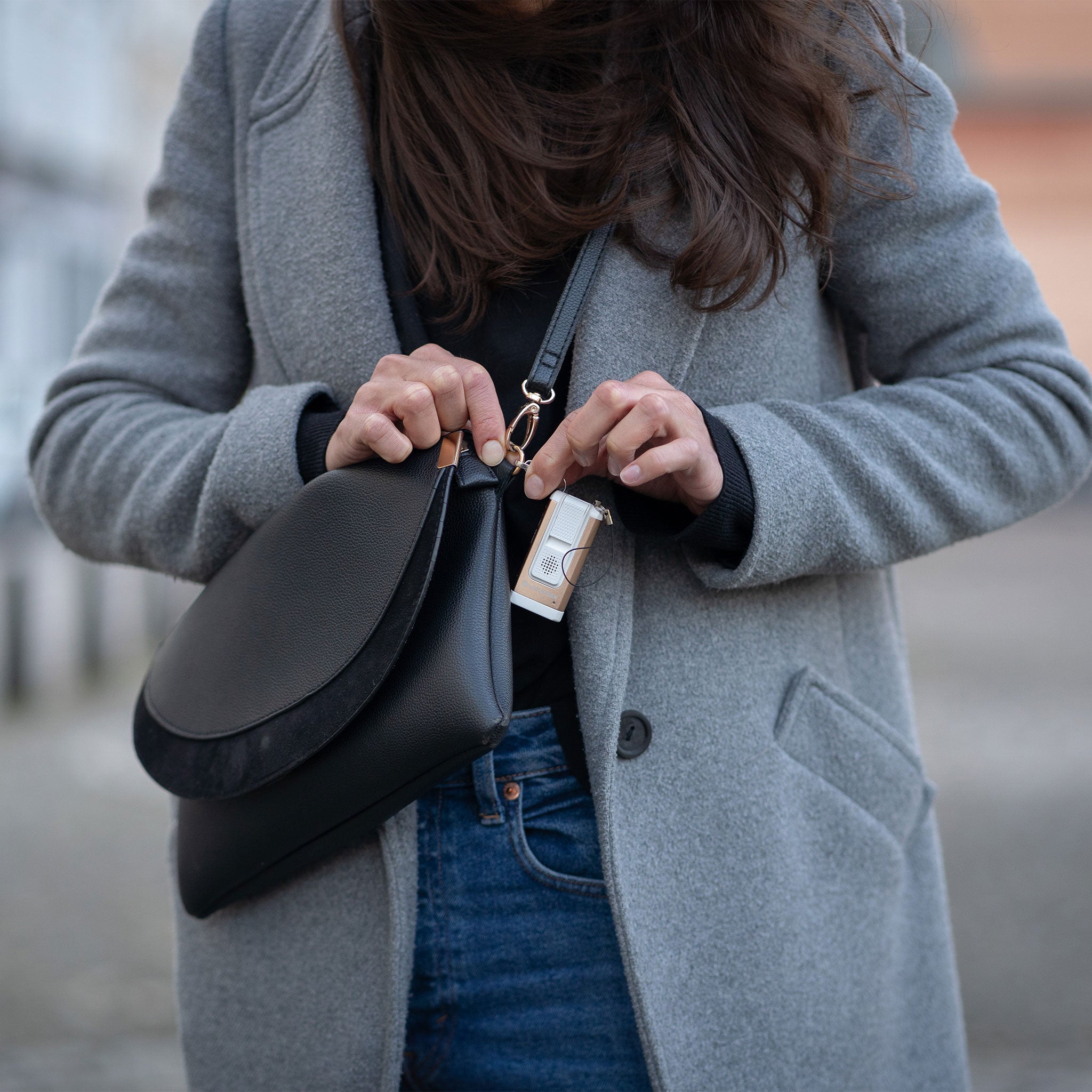 Ledlenser K6R Safety Keychain Light attached to a bag strap as a person holds it a compact rechargeable keyring flashlight on a grey coat and black bag