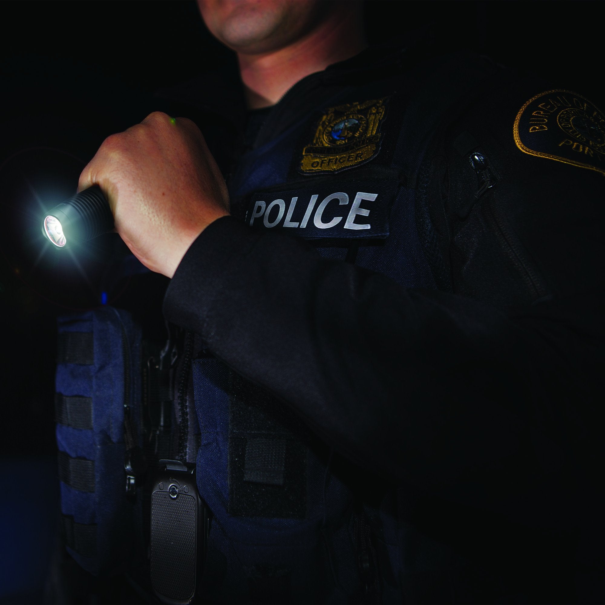 Ledlenser F1 Torch held by a police officer in a tactical vest with the beam visible in darkness