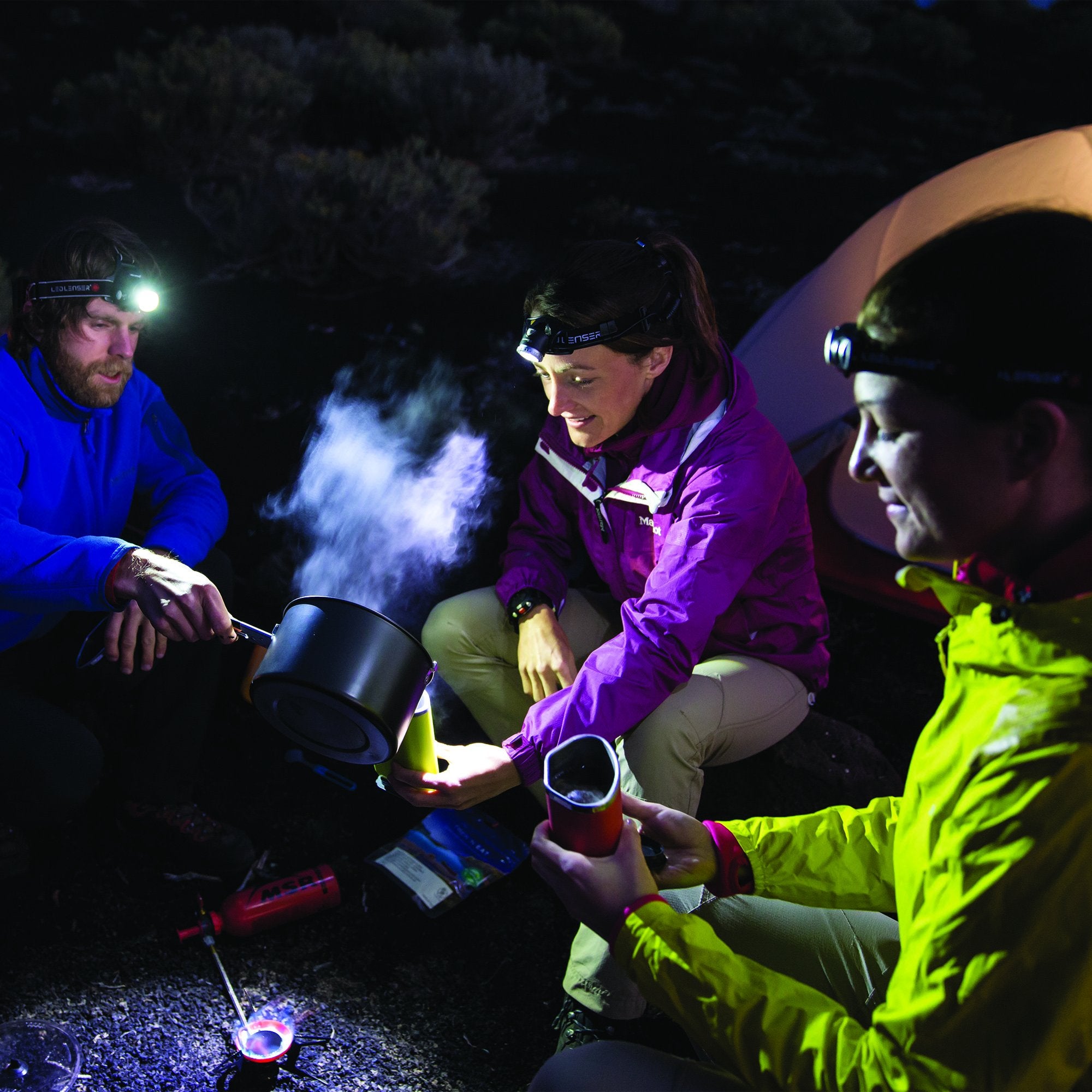 H14R 2 Headlamp worn by the central camper during a nighttime outdoor scene with two others headlamps lit near a tent and cooking gear