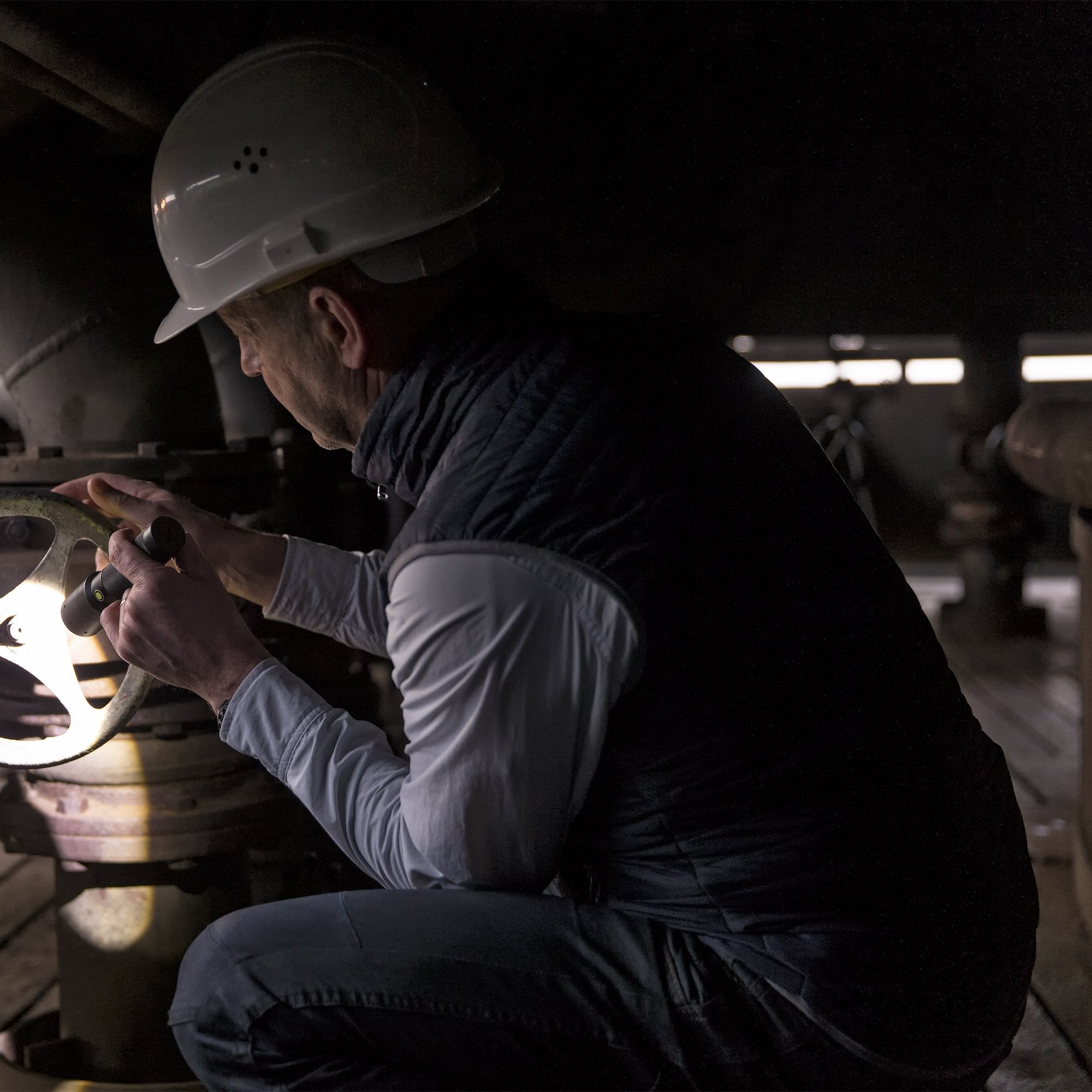 i9R Rechargeable Torch held by a worker in a white hard hat inspecting an industrial valve in a dim workspace