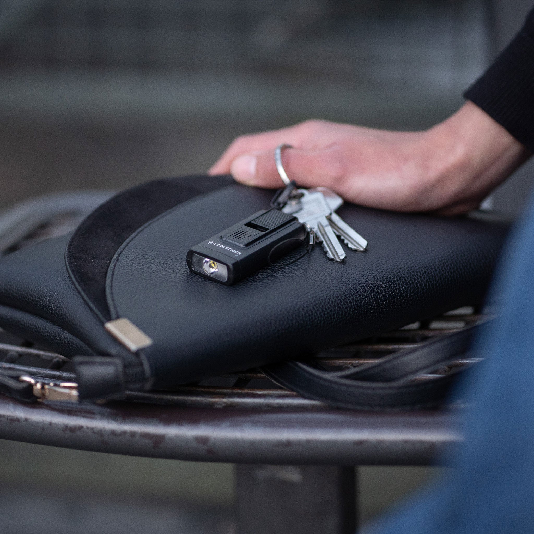 Ledlenser K6R 4GB Keychain Light compact black keychain torch with attached keys resting on a black bag surface hand in frame