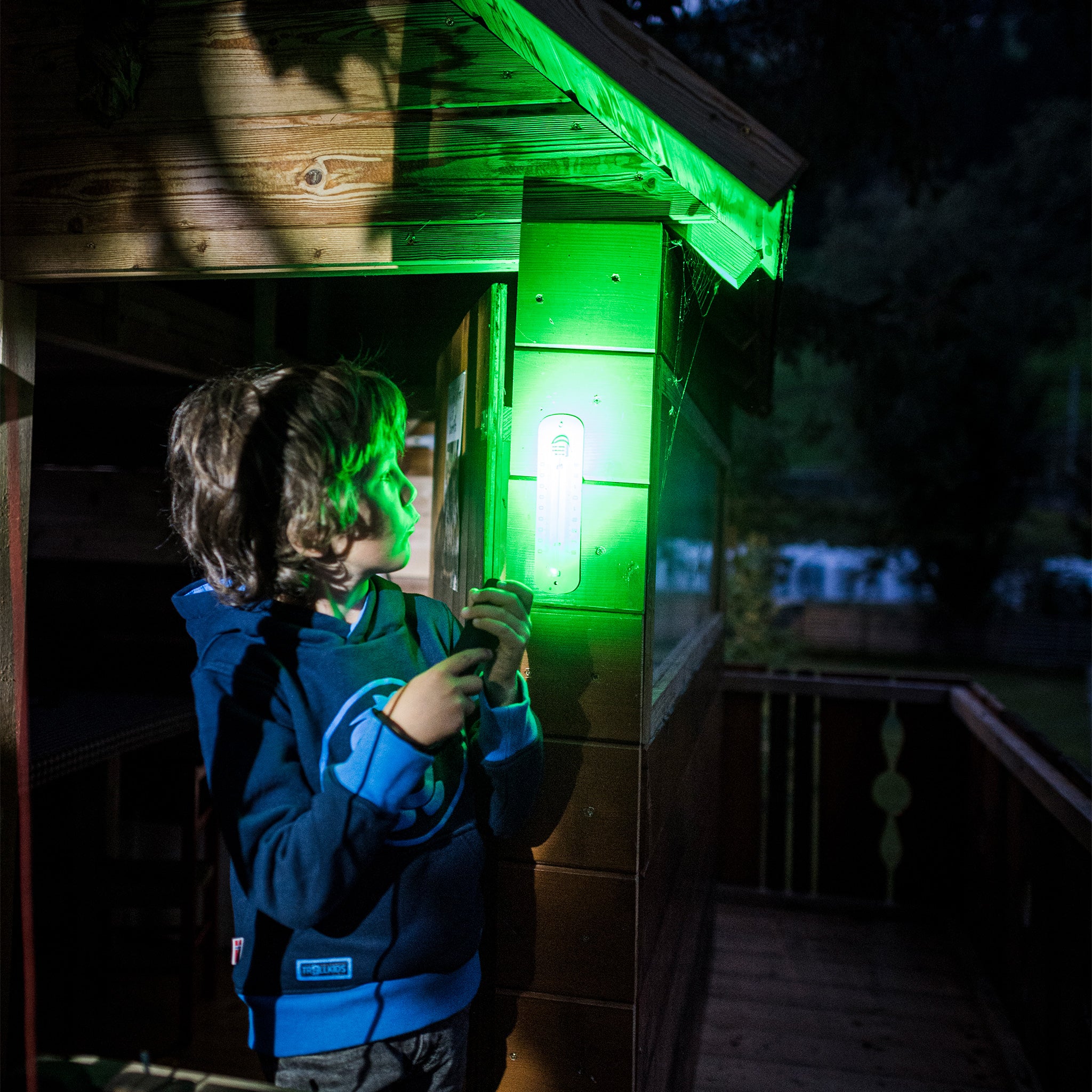 Ledlenser Kidbeam4 Torch held by a child on a wooden cabin porch with a green glow on the wall