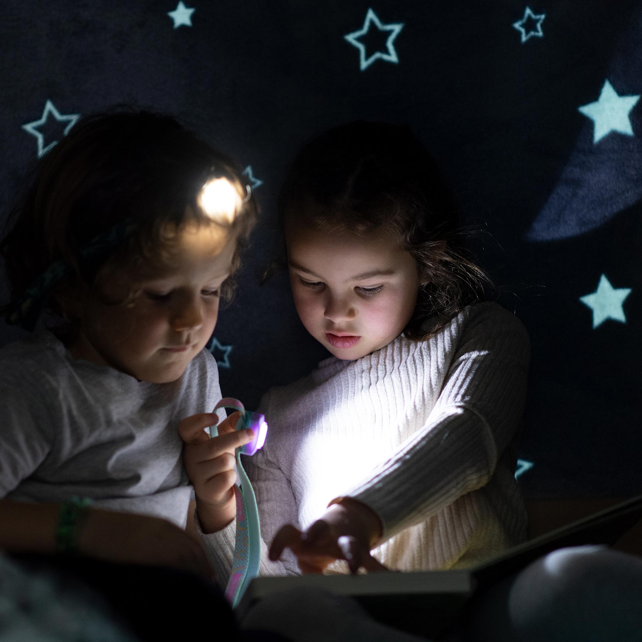 Kidled2 Headlamp worn by a child in a dark room with another child glow from headlamp lighting a book