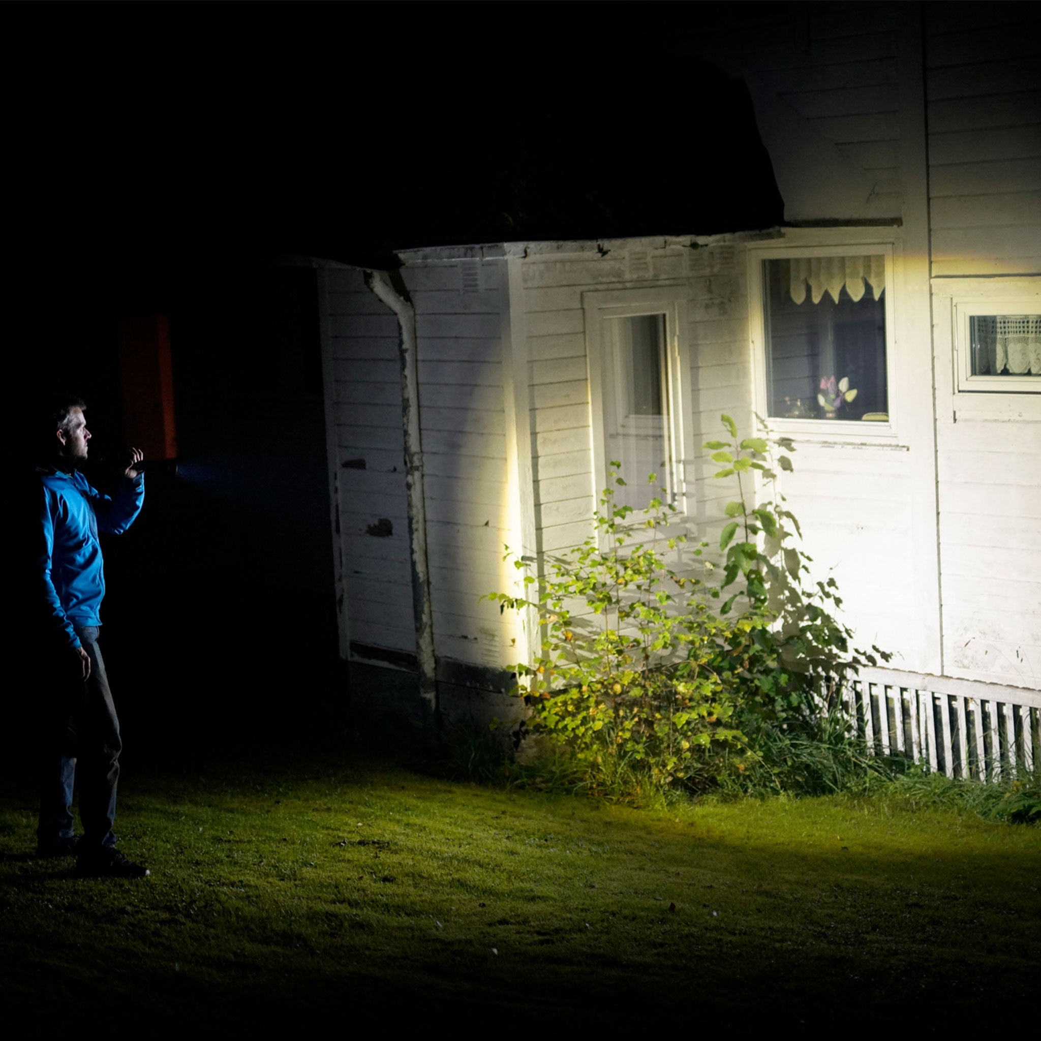 P17R Core Torch handheld light directed at a white house exterior at night person in a blue jacket holding the beam