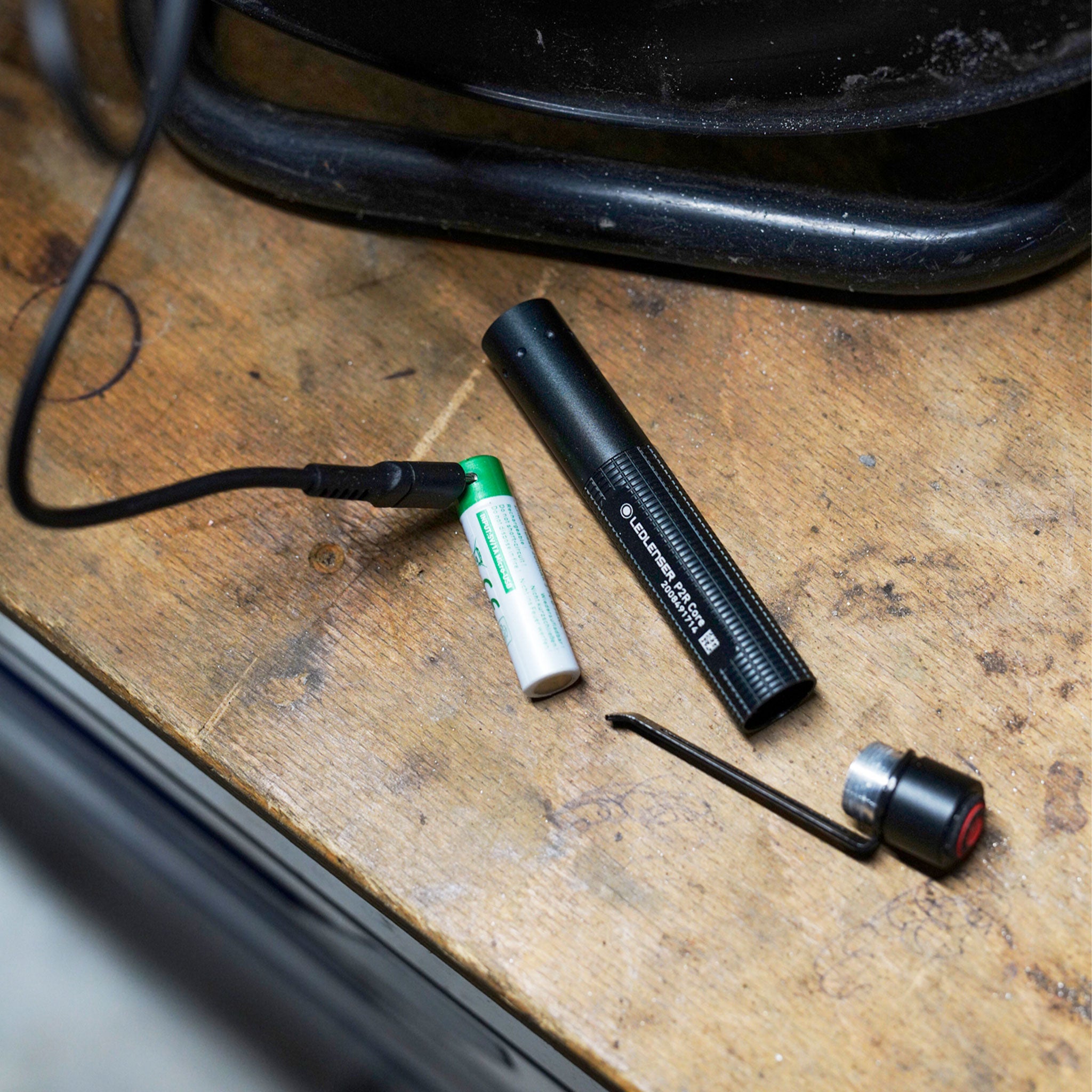 Ledlenser P2R Core Torch disassembled on a wooden work surface with a green rechargeable battery and a small connector accessory