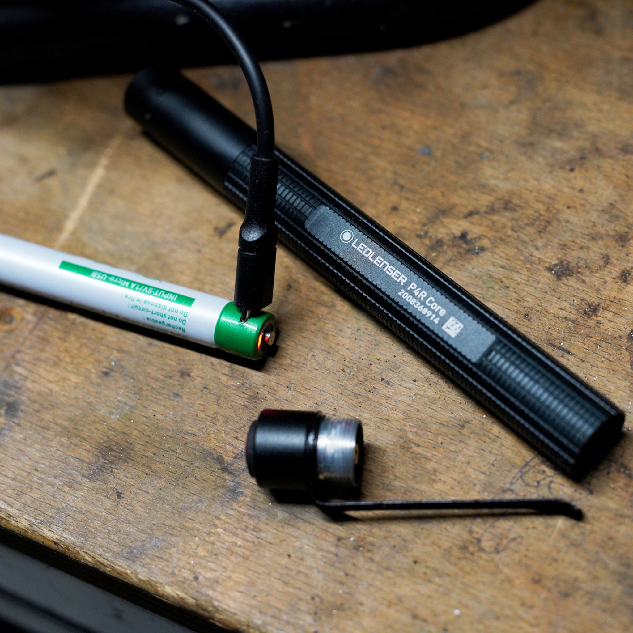 Ledlenser P4R Core Torch on a workbench with charging cable attached to its green end cap and a black protective case nearby