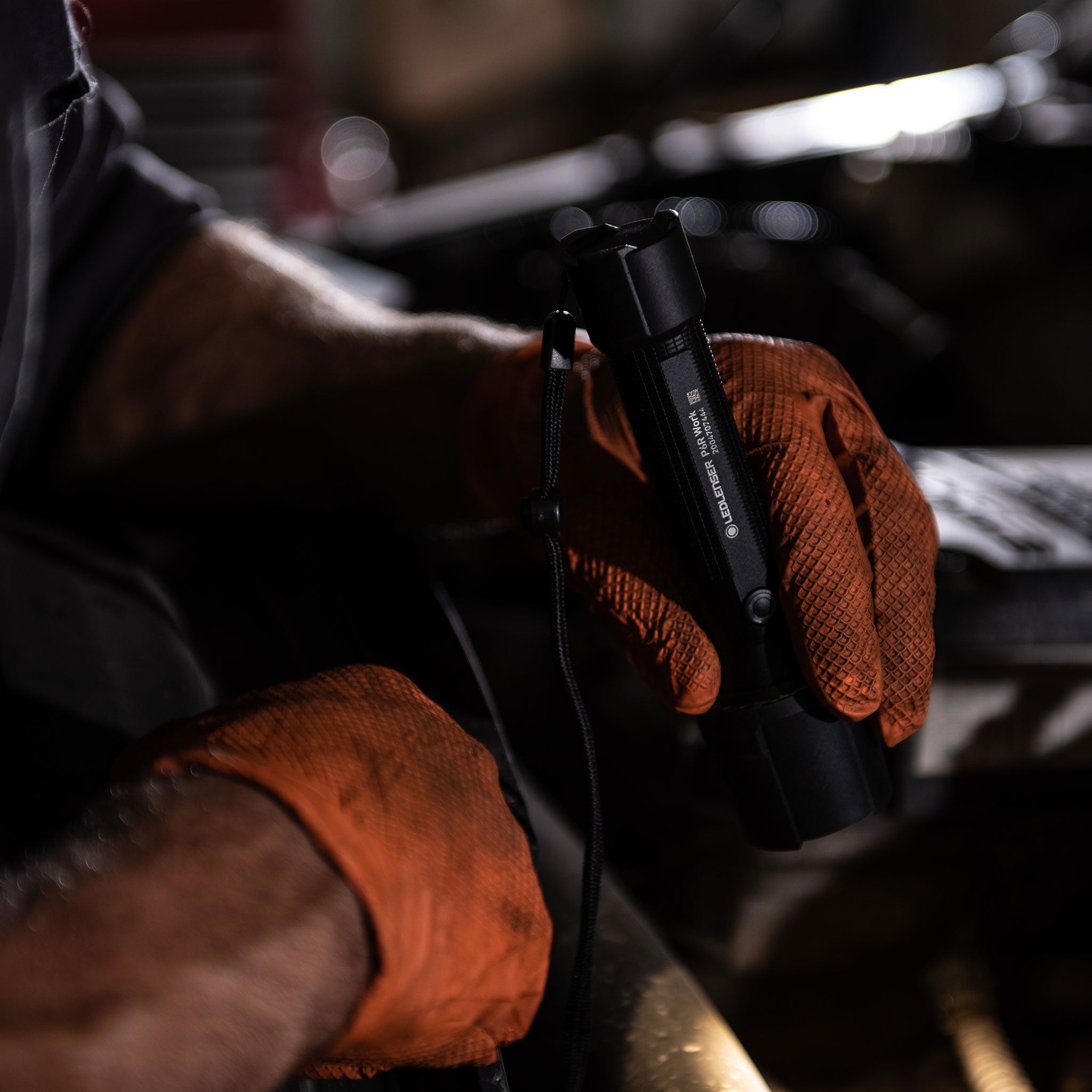Ledlenser P5R Work Torch held in gloved hands at a workshop compact black rechargeable flashlight with wrist strap