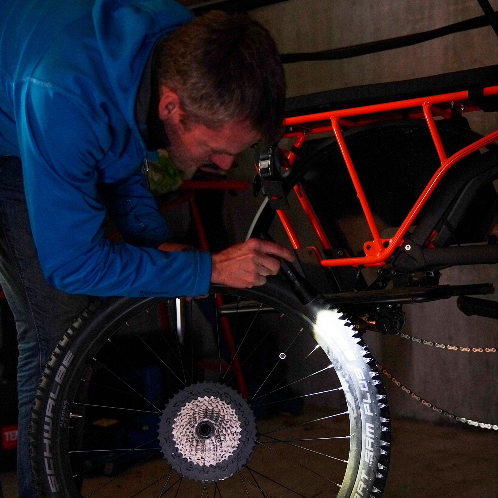 Ledlenser P6R Core Torch in use by a person inspecting a bike frame in a workshop showing a rear wheel with an orange frame and the mounted light