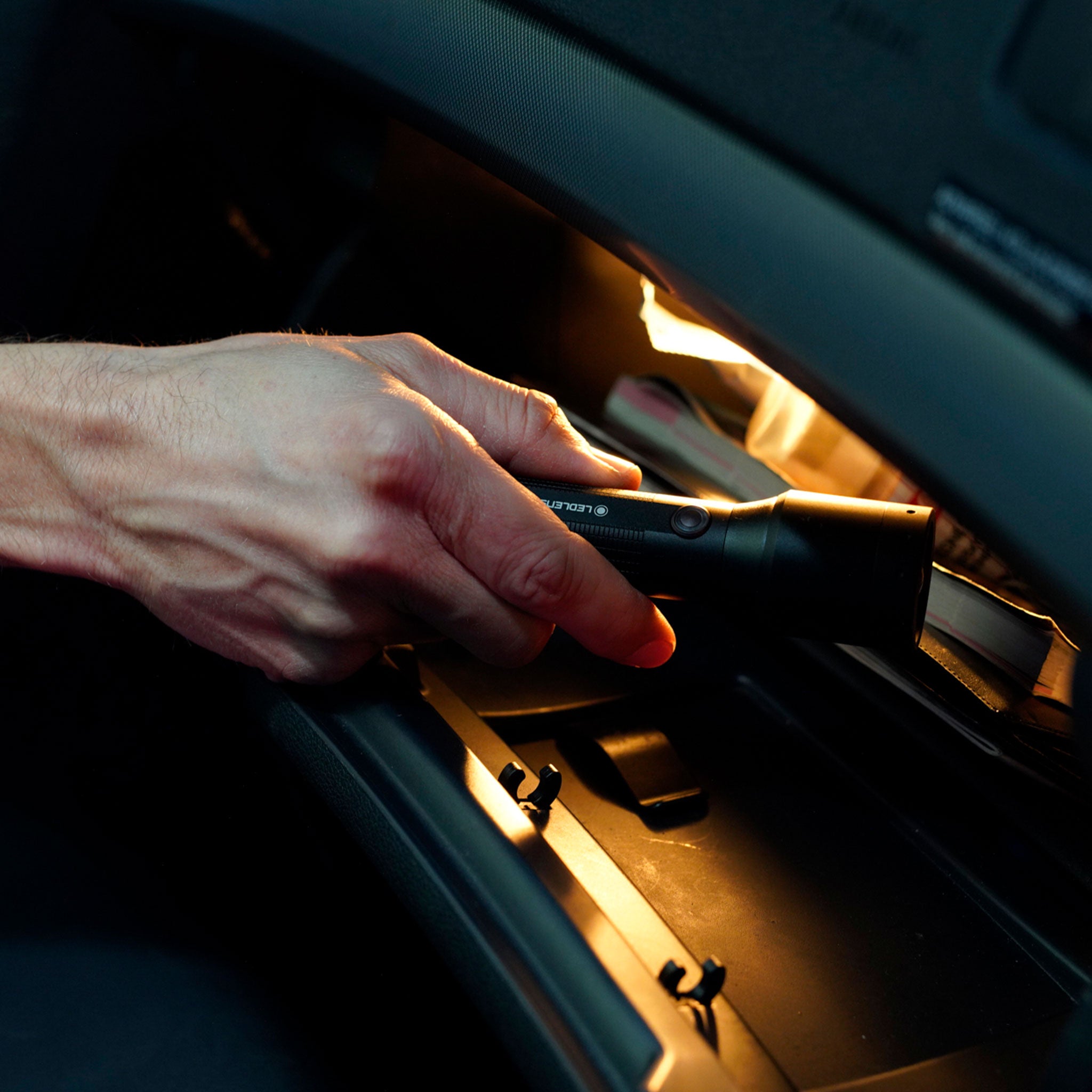 Ledlenser P6R Core Torch held by a hand inside a car central console area with warm interior lighting