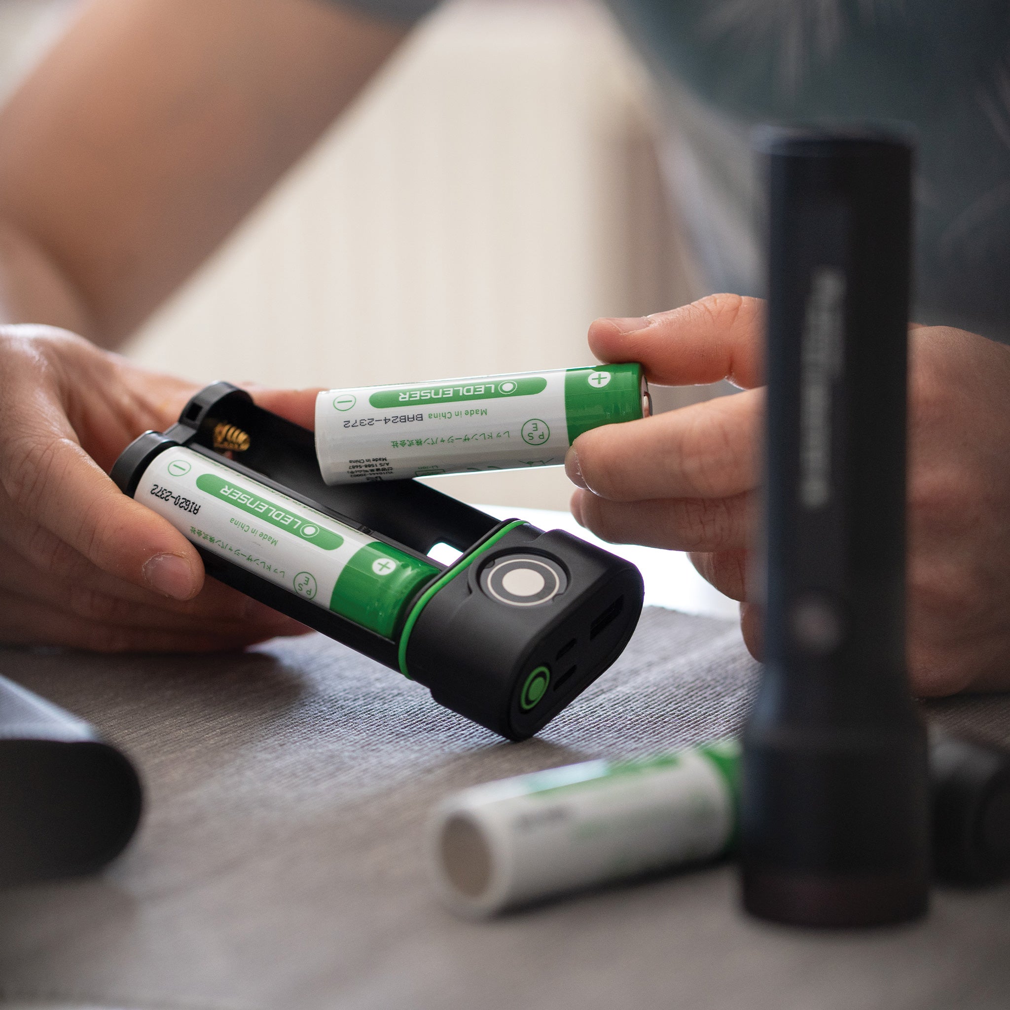 Flex10 Powerbank with two green battery cells being inserted into its black charging unit hands handling batteries on a table