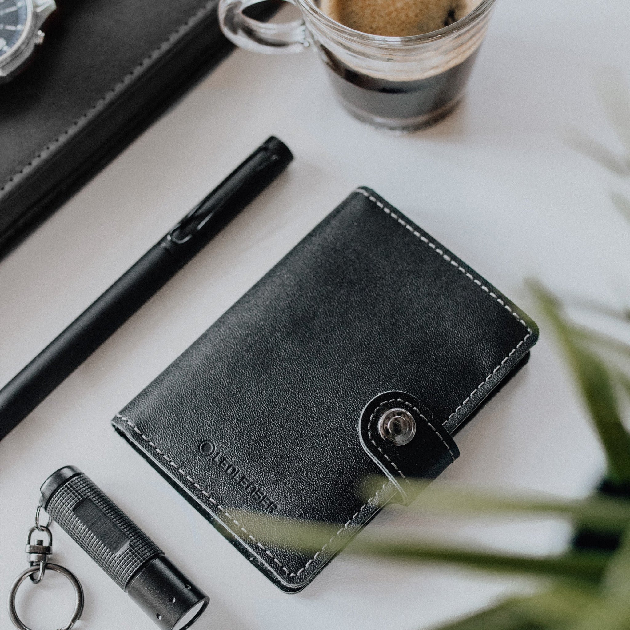 Lite Wallet® black leather wallet with snap closure on a desk with a pen and key fob nearby product in use
