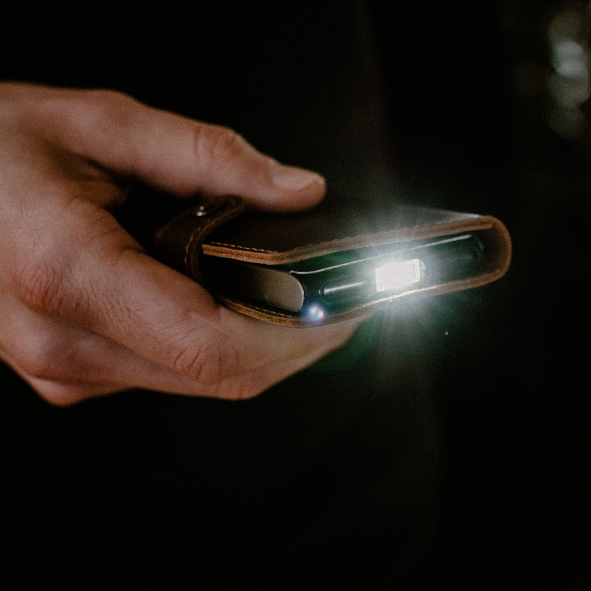 Ledlenser Lite Wallet® leather wallet held in a hand with a small LED light on its edge glowing in a dark background