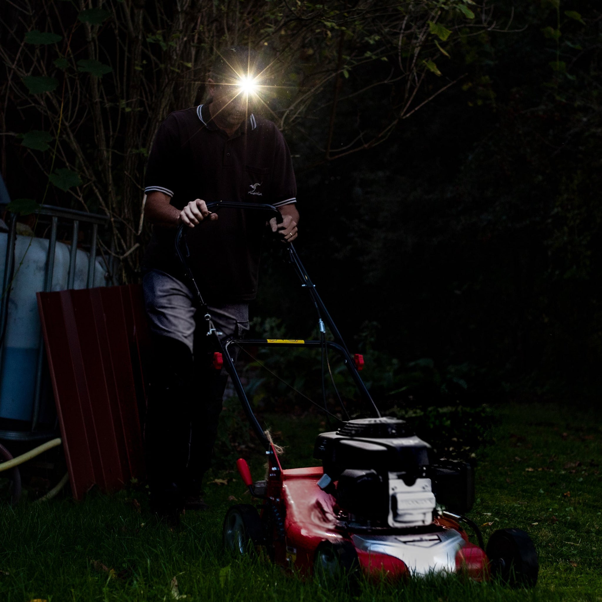 Ledlenser MH4 Powercase Combo headlamp with charging case worn by a person outdoors at dusk beam shining ahead near a lawn mower