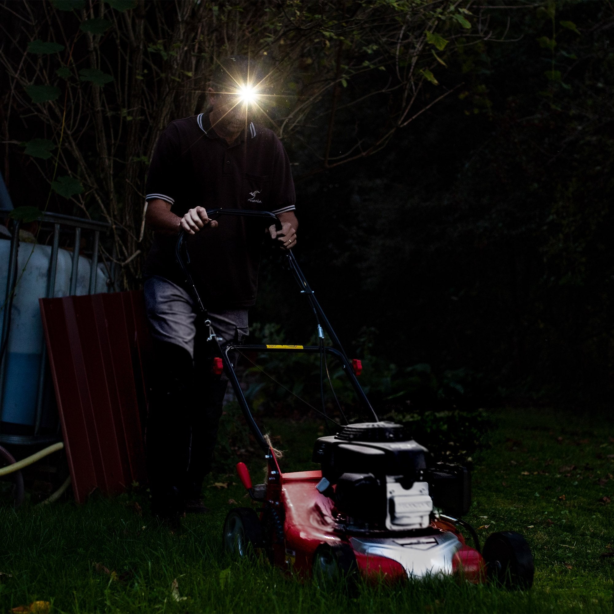 MH4 Black Battery Operated Torch seen on a person in a dark garden headlamp beam shining as they push a red lawn mower