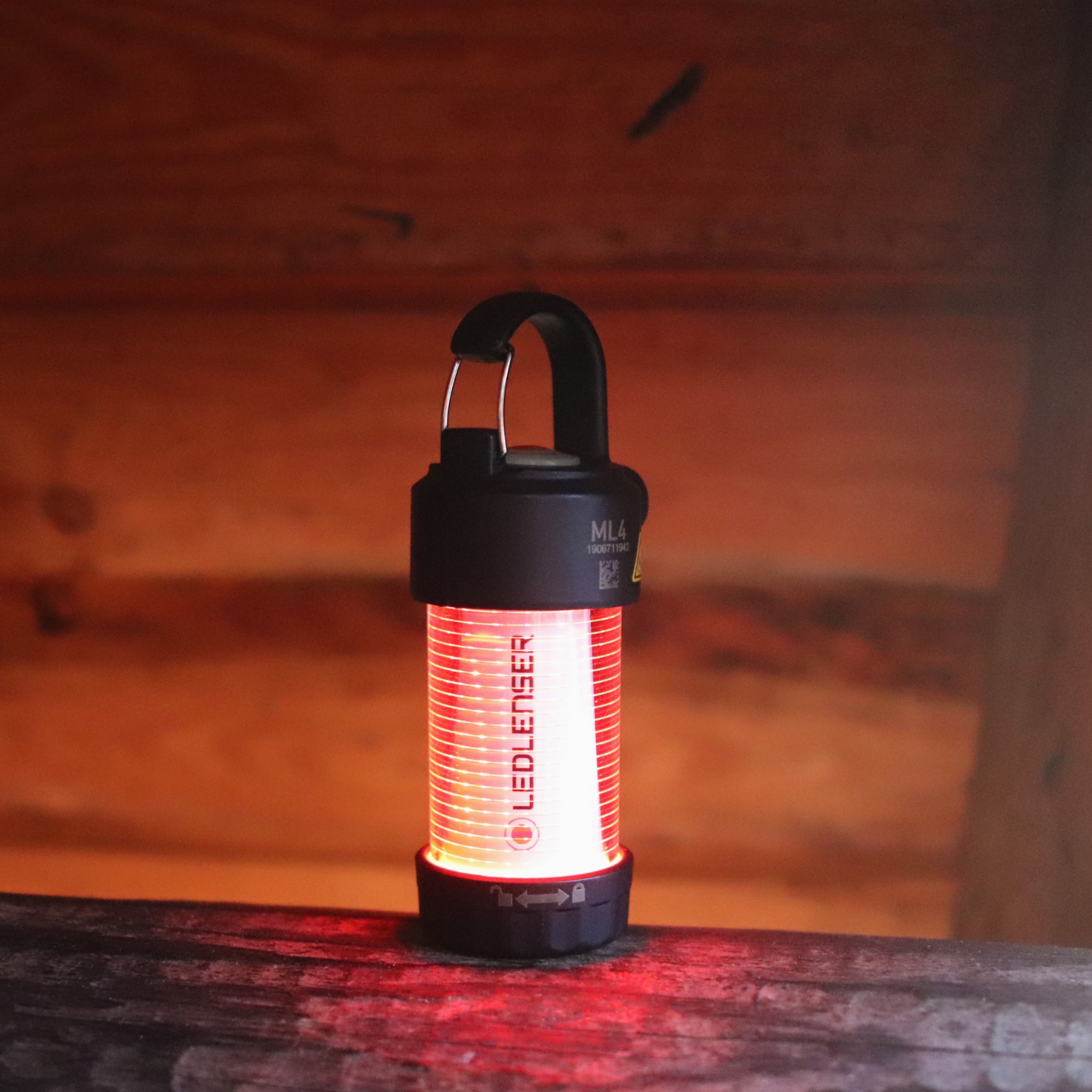 ML4 Lantern: black cylindrical lantern with red glow hanging handle on top Ledlenser branding on the body resting on a wooden surface