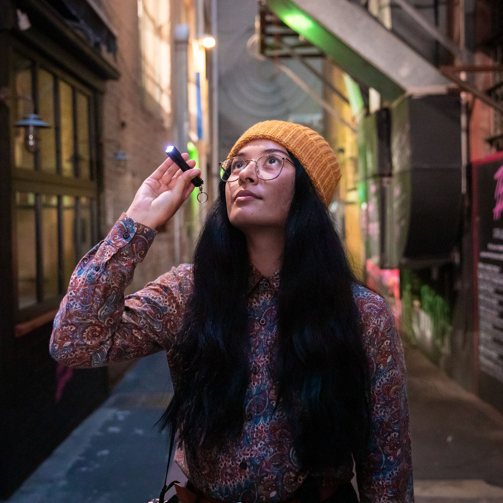P3 Battery Operated Torch held by a woman in an orange beanie in a dim urban alley with the torch lit and blue glow