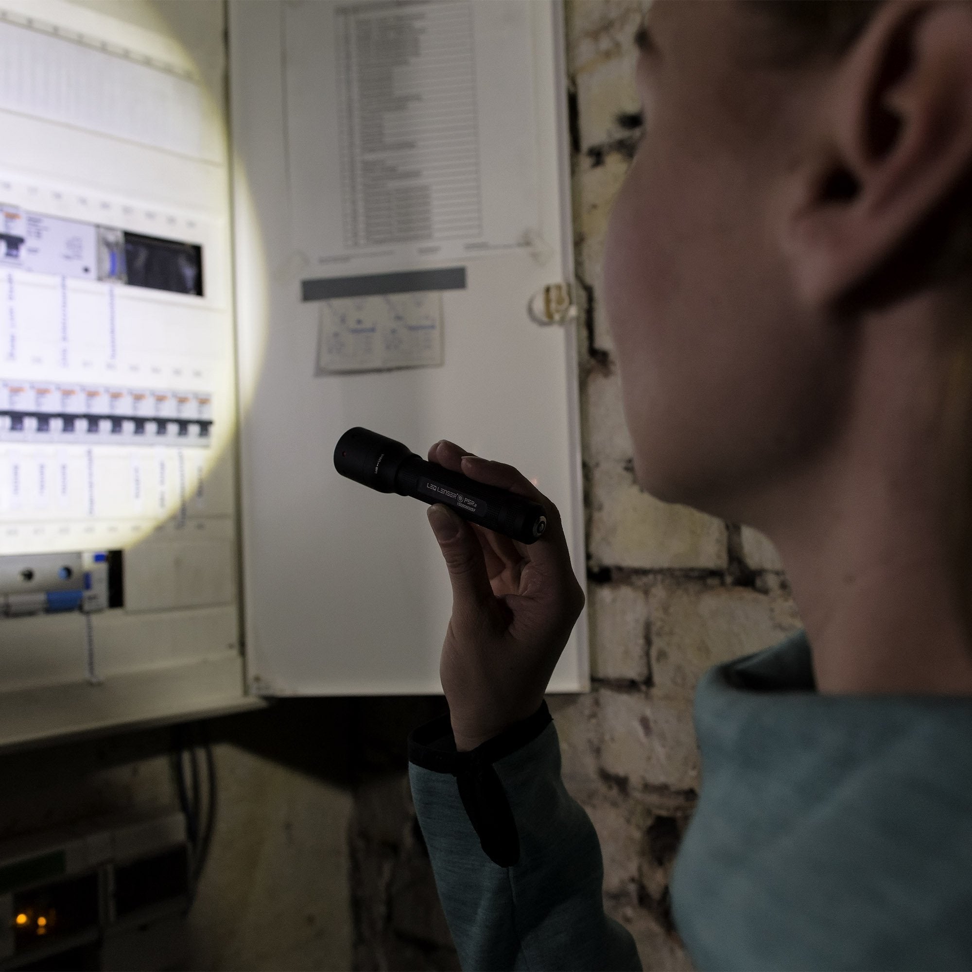P5R Torch held in a hand near an electrical panel in a dim workshop a compact black Ledlenser flashlight