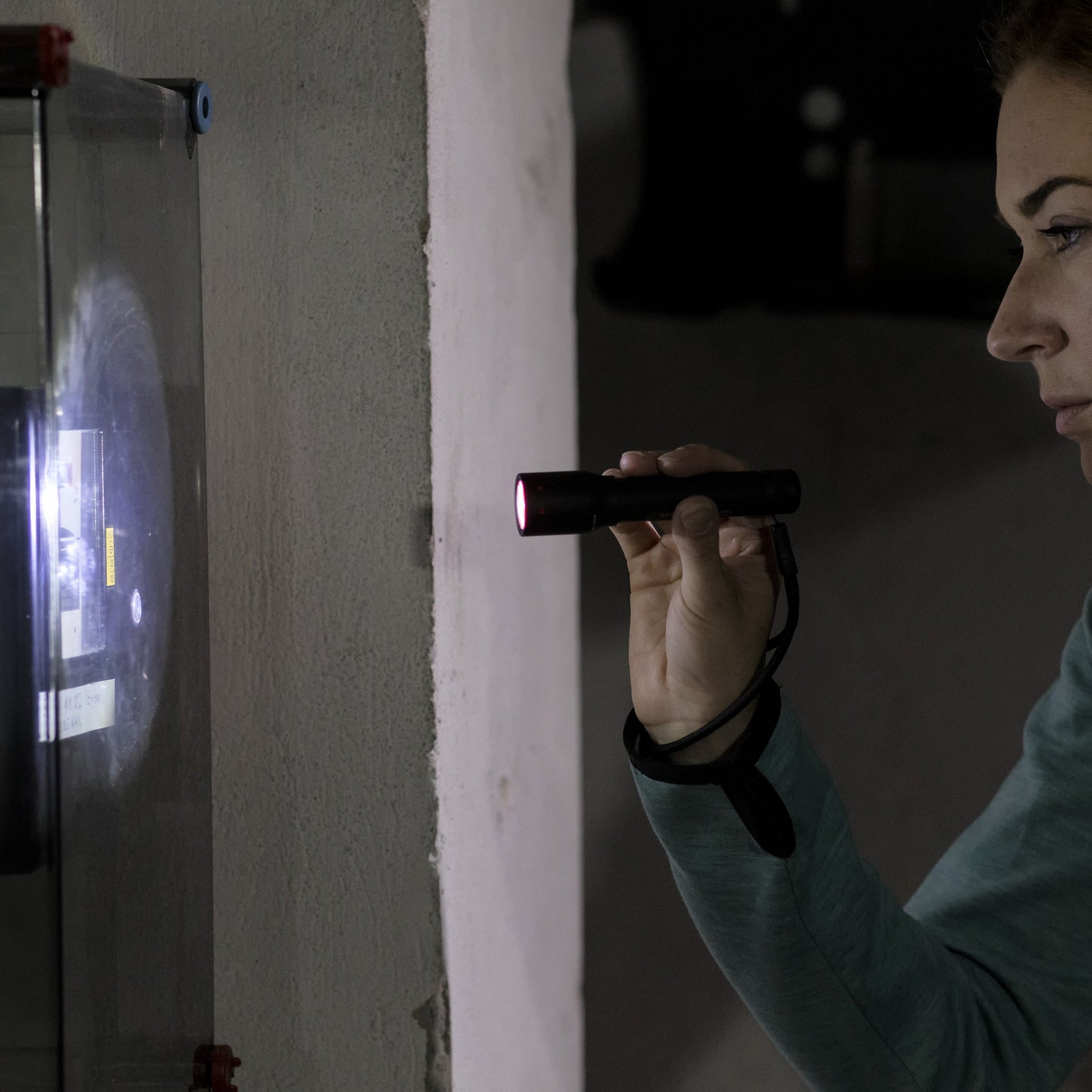 P5 Torch held by a person in a teal sleeve a small black flashlight with a red front light in a dim industrial setting
